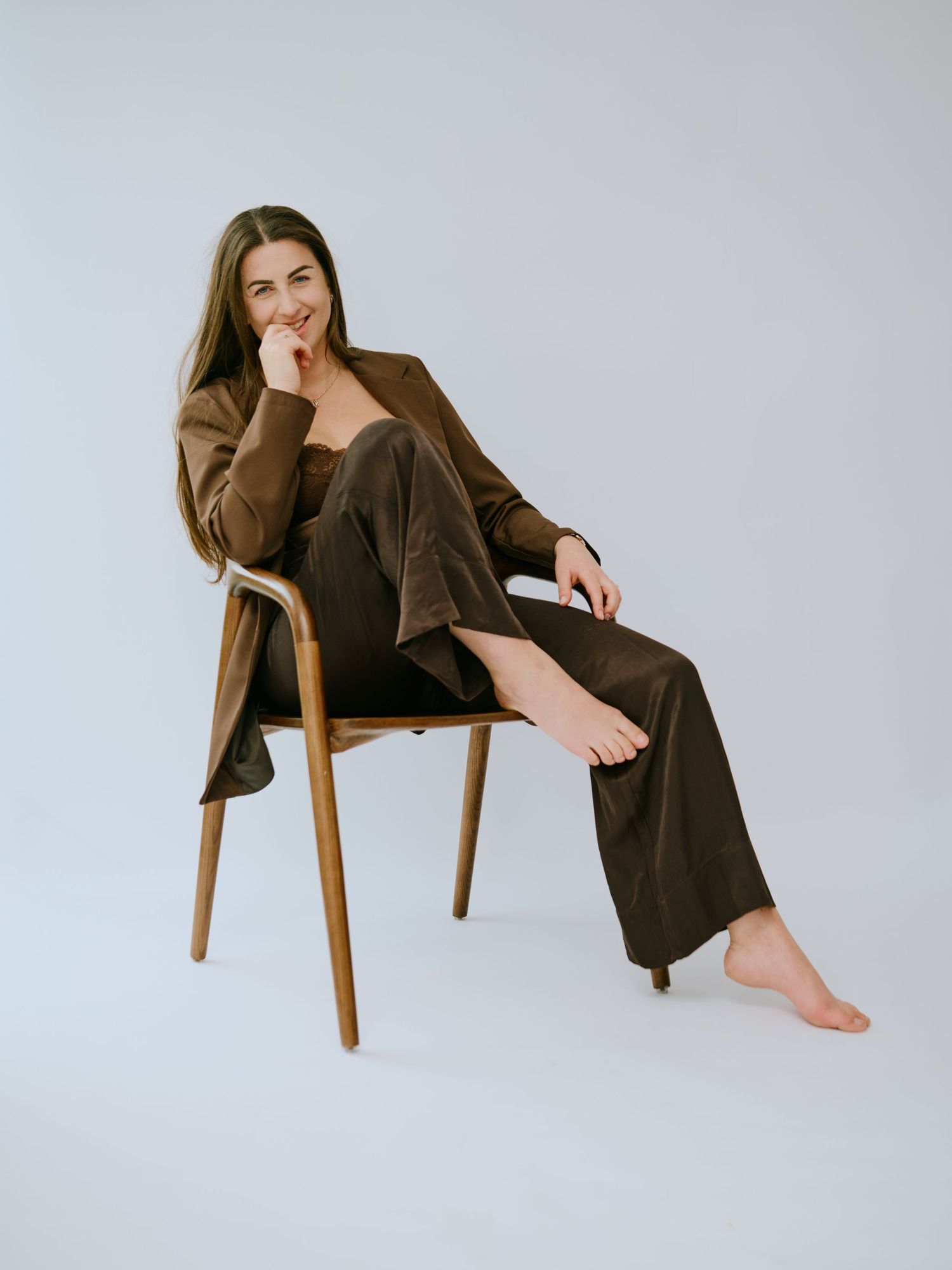 A person in a brown sweater sits casually on a wooden chair against a white background in three different poses.
