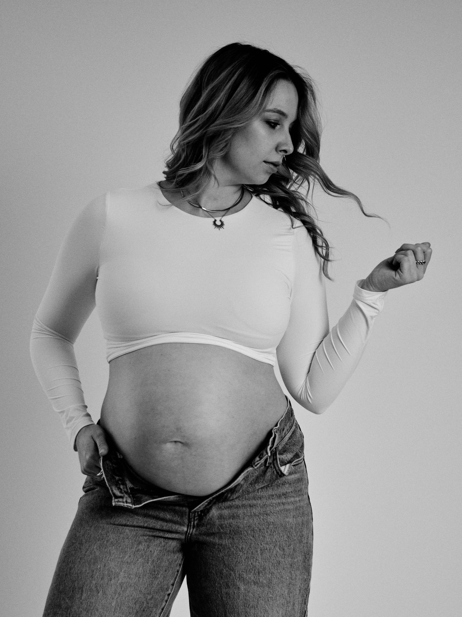 Black and white fashion photo series showing a model in jeans and white top posing against a plain background.