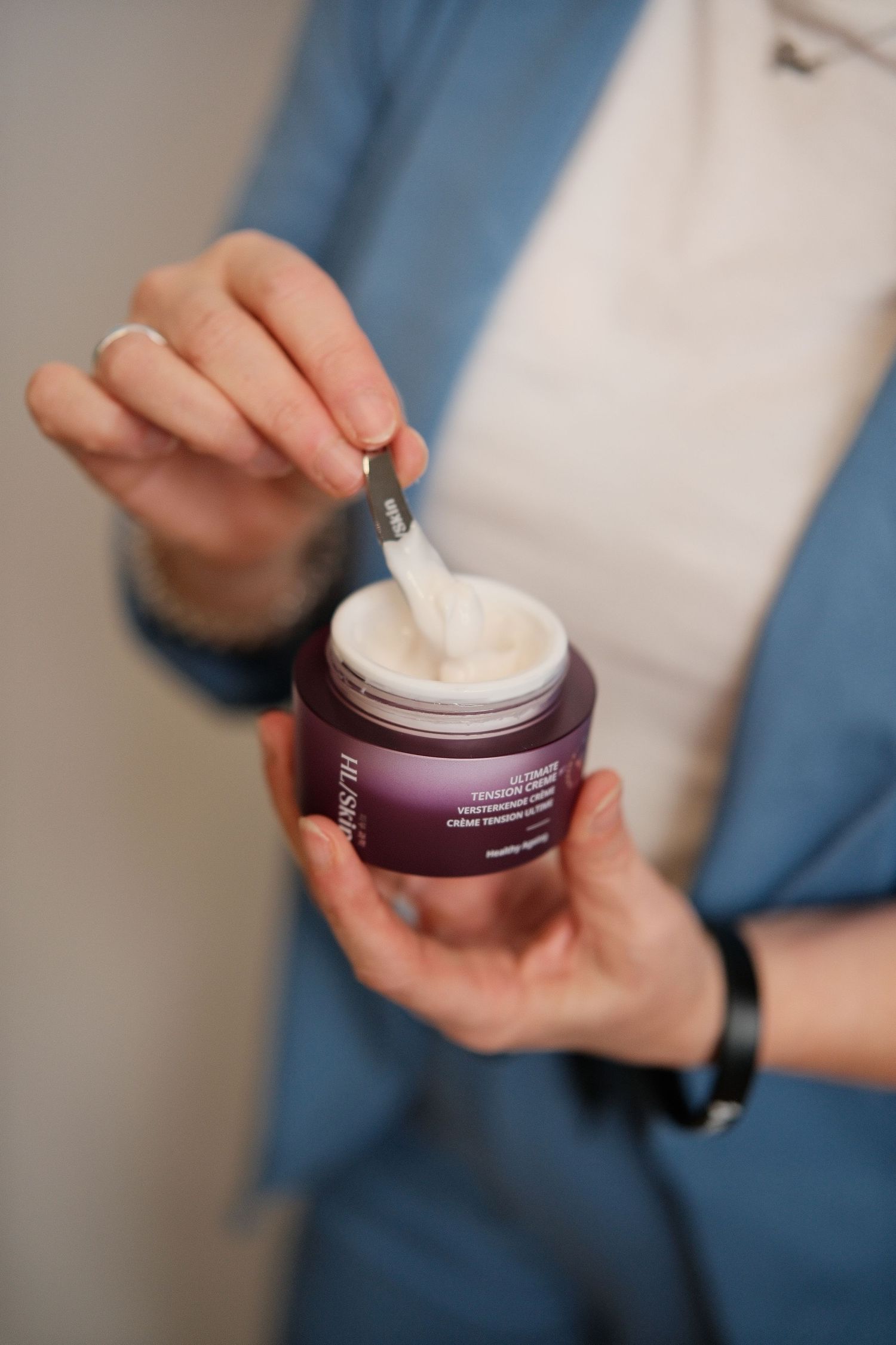Hands holding and opening a purple skincare cream jar.