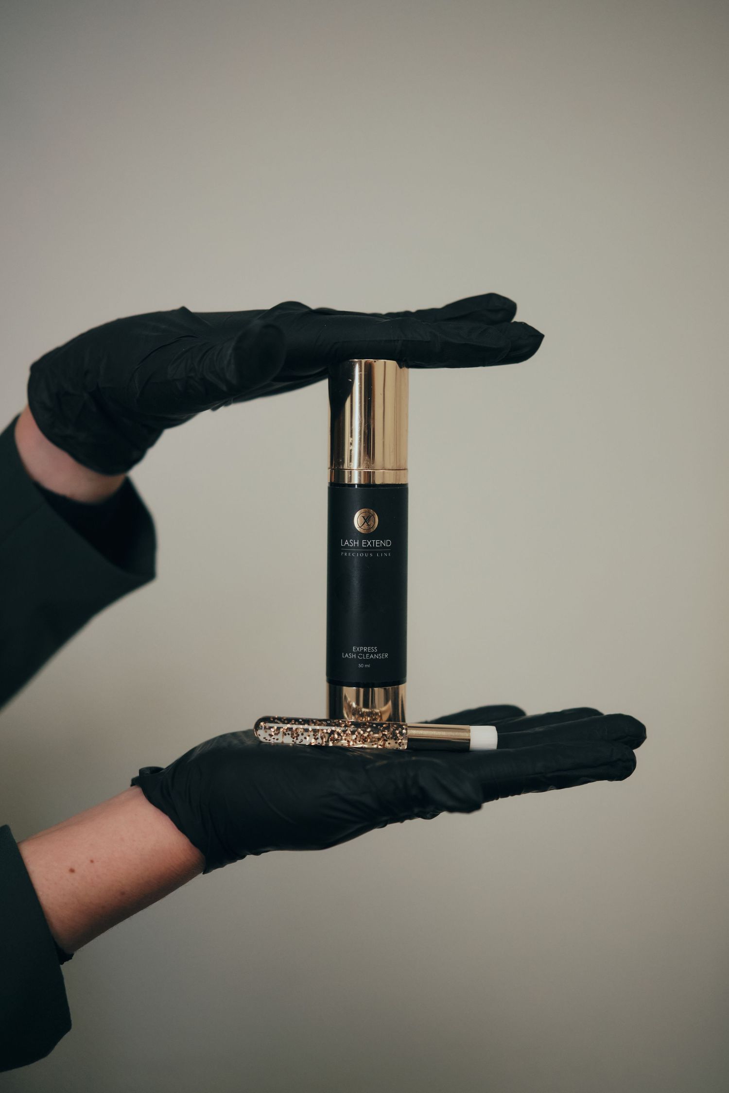 Hands in black gloves holding a luxury black and gold skincare serum bottle with a decorative applicator tool.