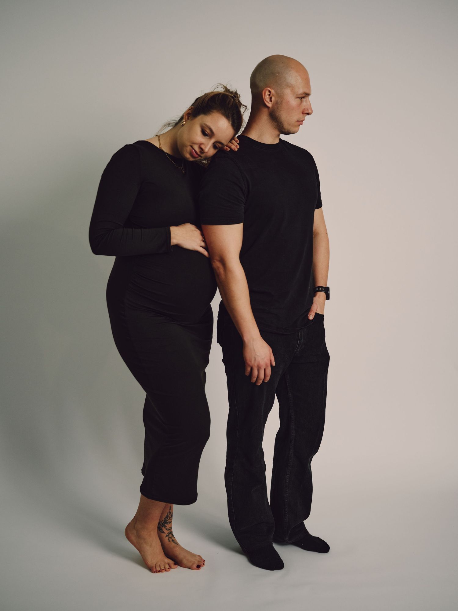 Two figures in black clothing pose together against a light gray backdrop in a minimalist artistic series.
