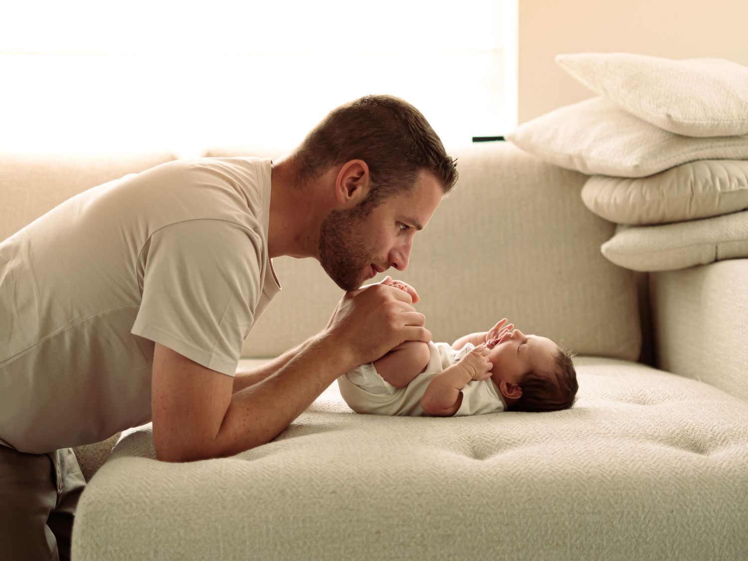 Parent and baby sharing tender moment on white couch in natural light.