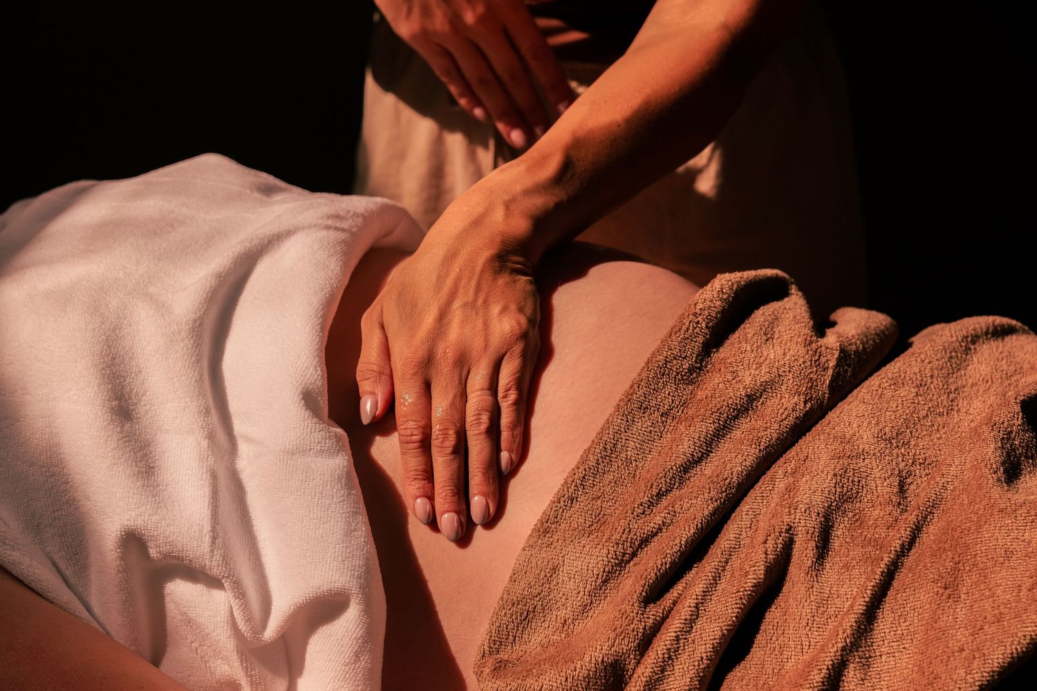 Hands performing a therapeutic massage on a person covered with a white sheet.