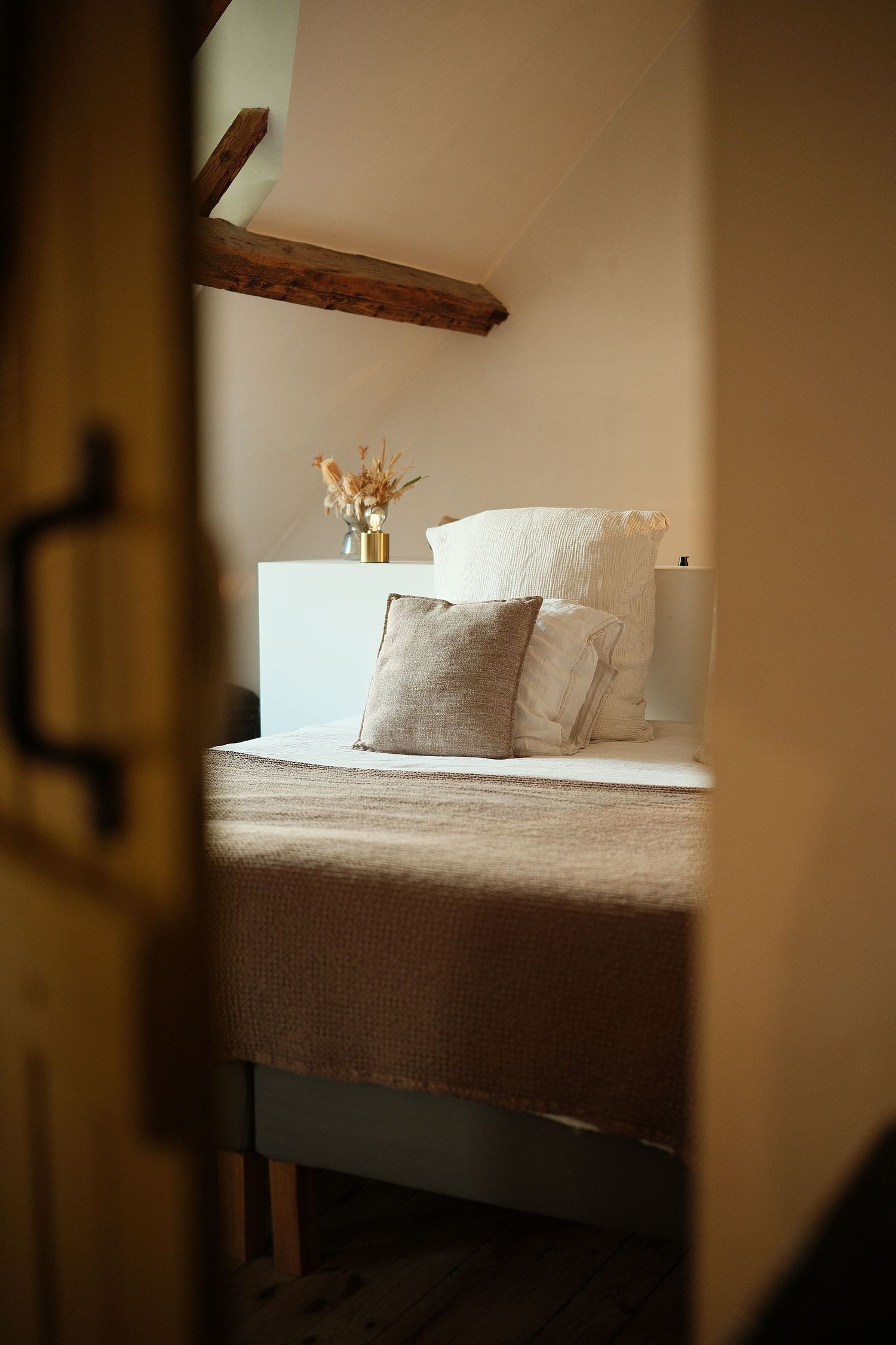 Cozy bed with white pillows and neutral bedding in soft lighting.