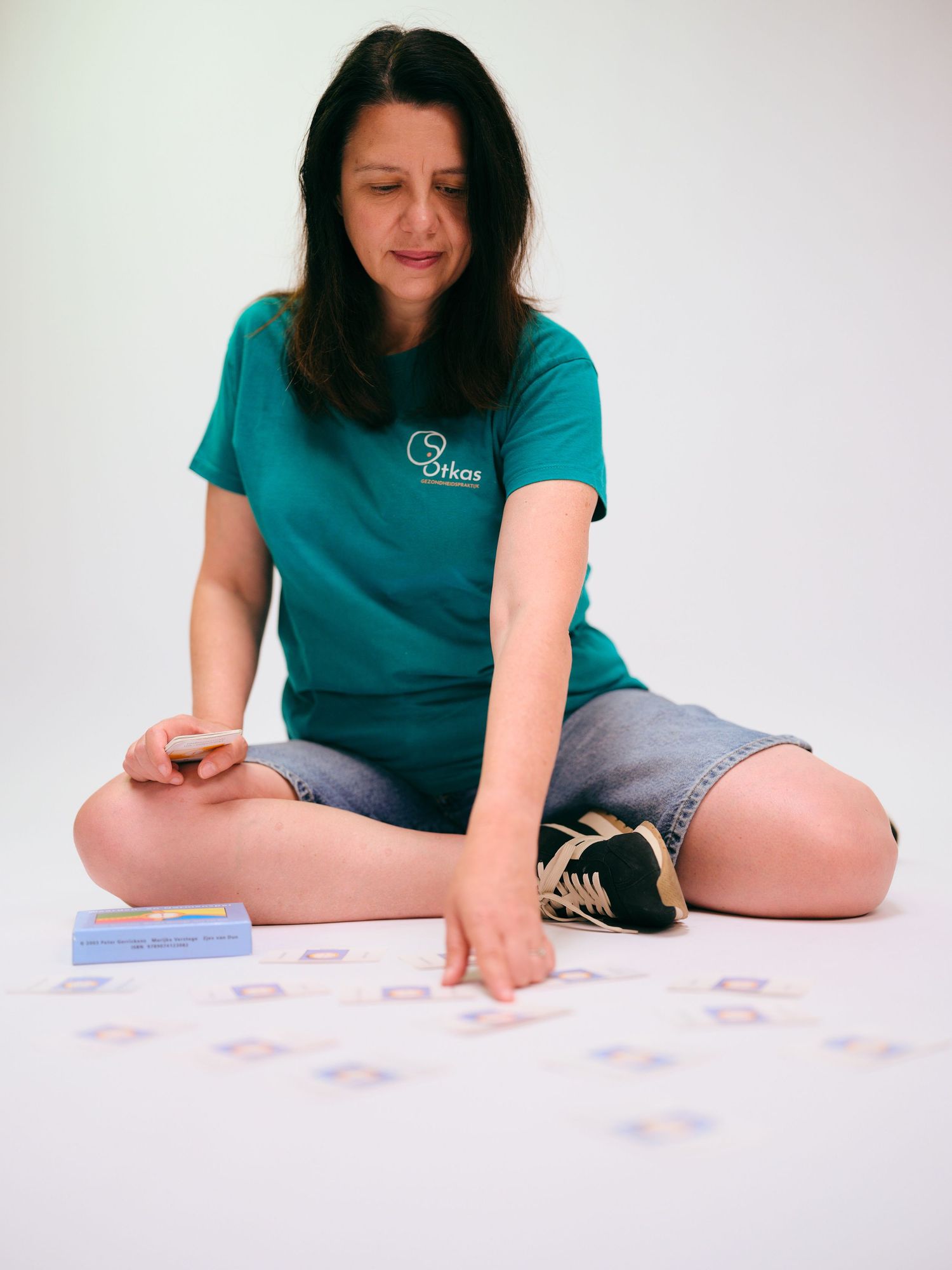 Woman in teal shirt sitting cross-legged on floor, arranging colorful cards in a pattern during a card game activity.
