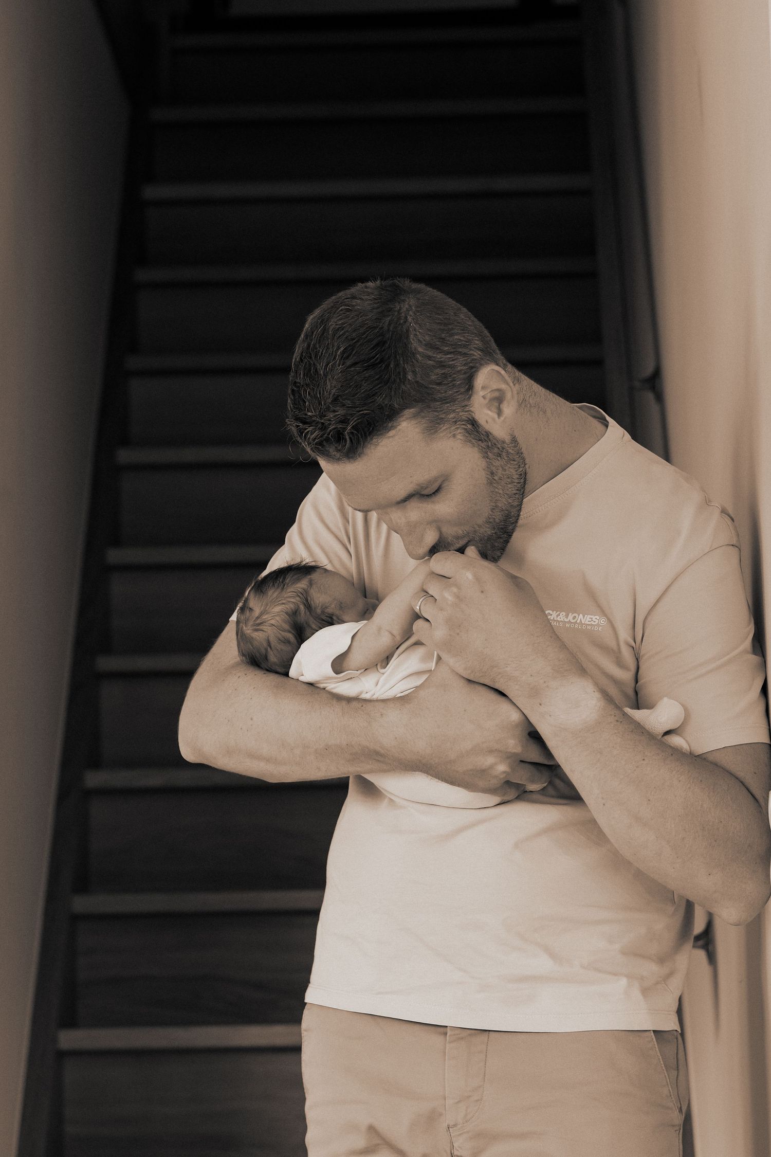 Emotional family moment captured in sepia tones against white wall.
