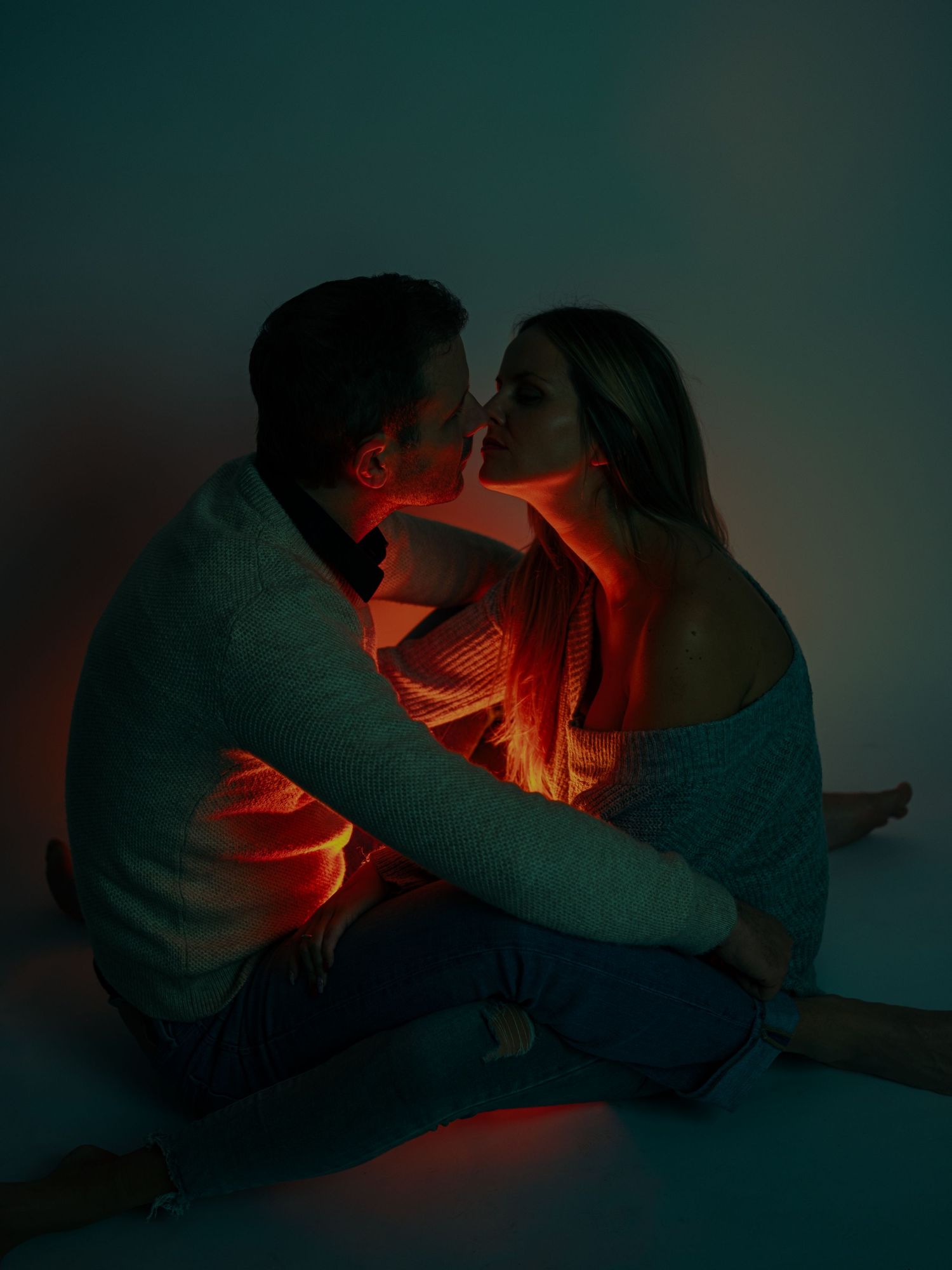 A romantic couple in silhouette sharing an intimate moment illuminated by dramatic red and teal lighting.
