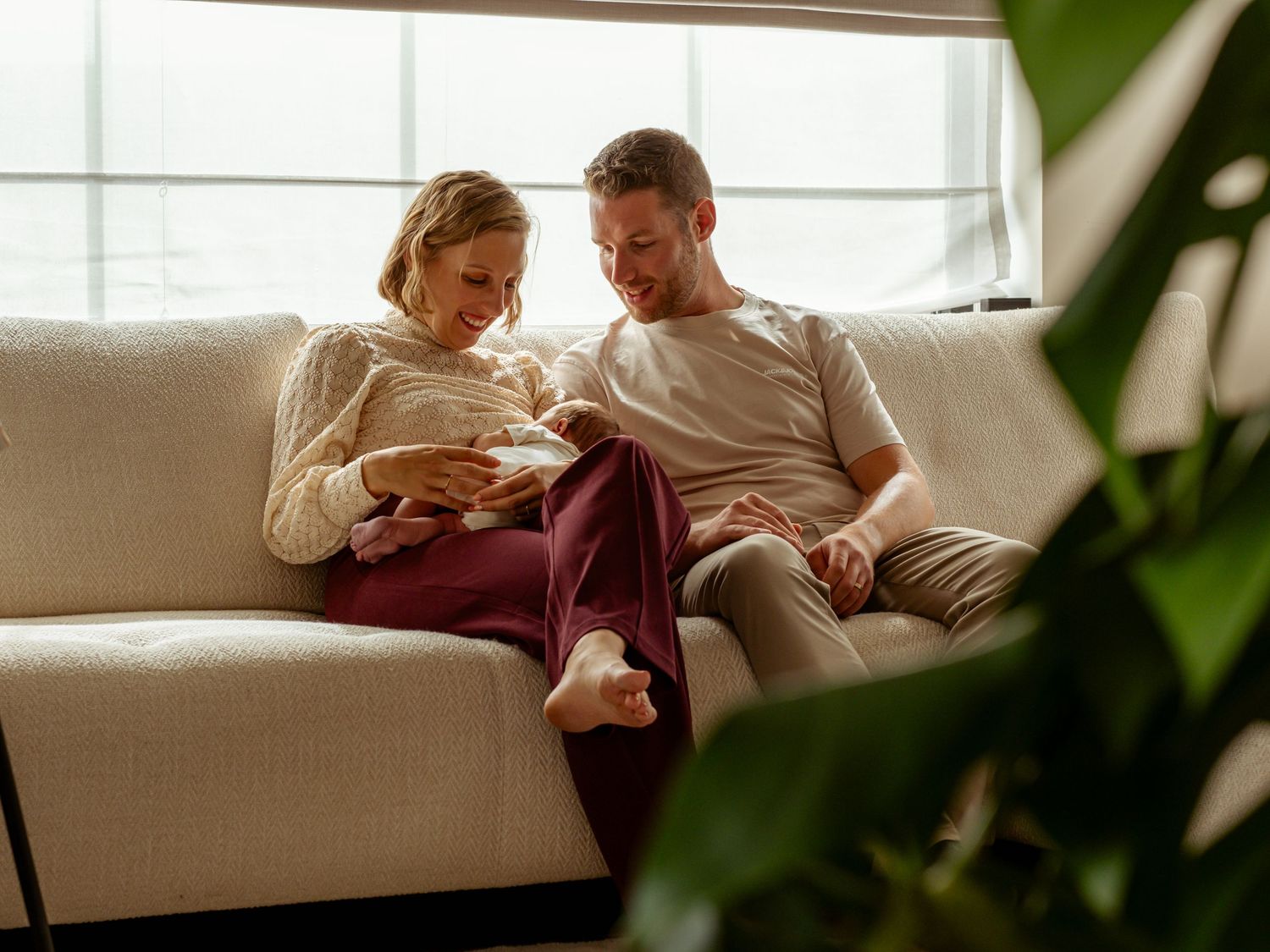 Couple sharing an intimate moment on a white sofa near a bright window.