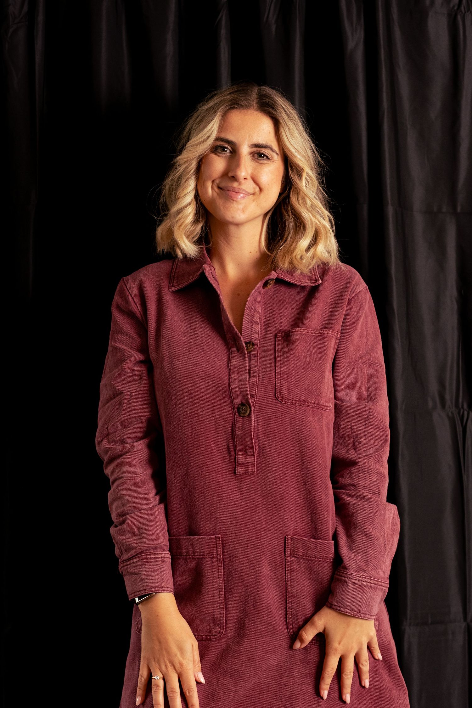 Person wearing burgundy corduroy shirt poses against black background in studio setting.