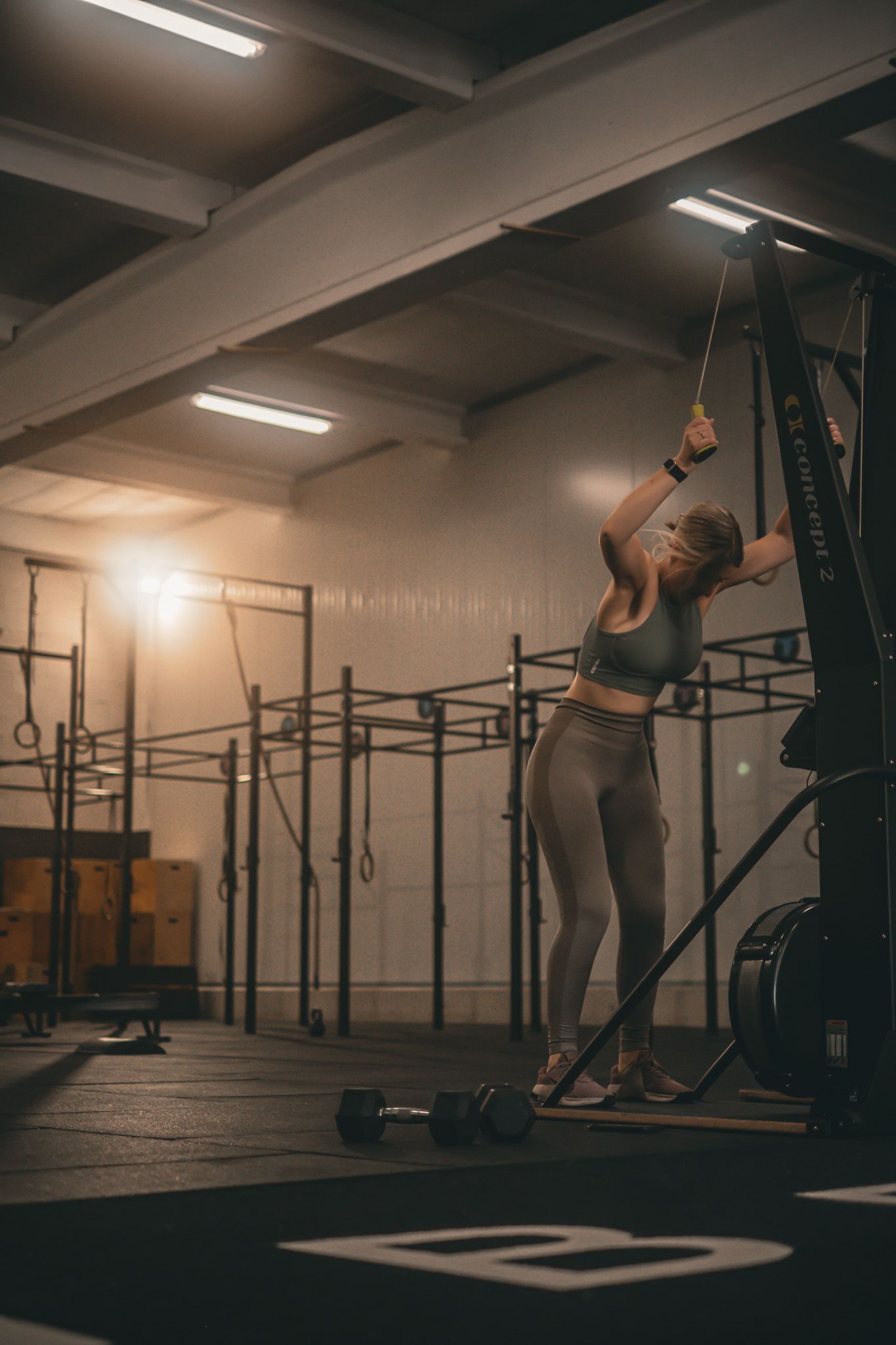 Athletic figure performing dynamic movements in dimly lit CrossFit gym setting.