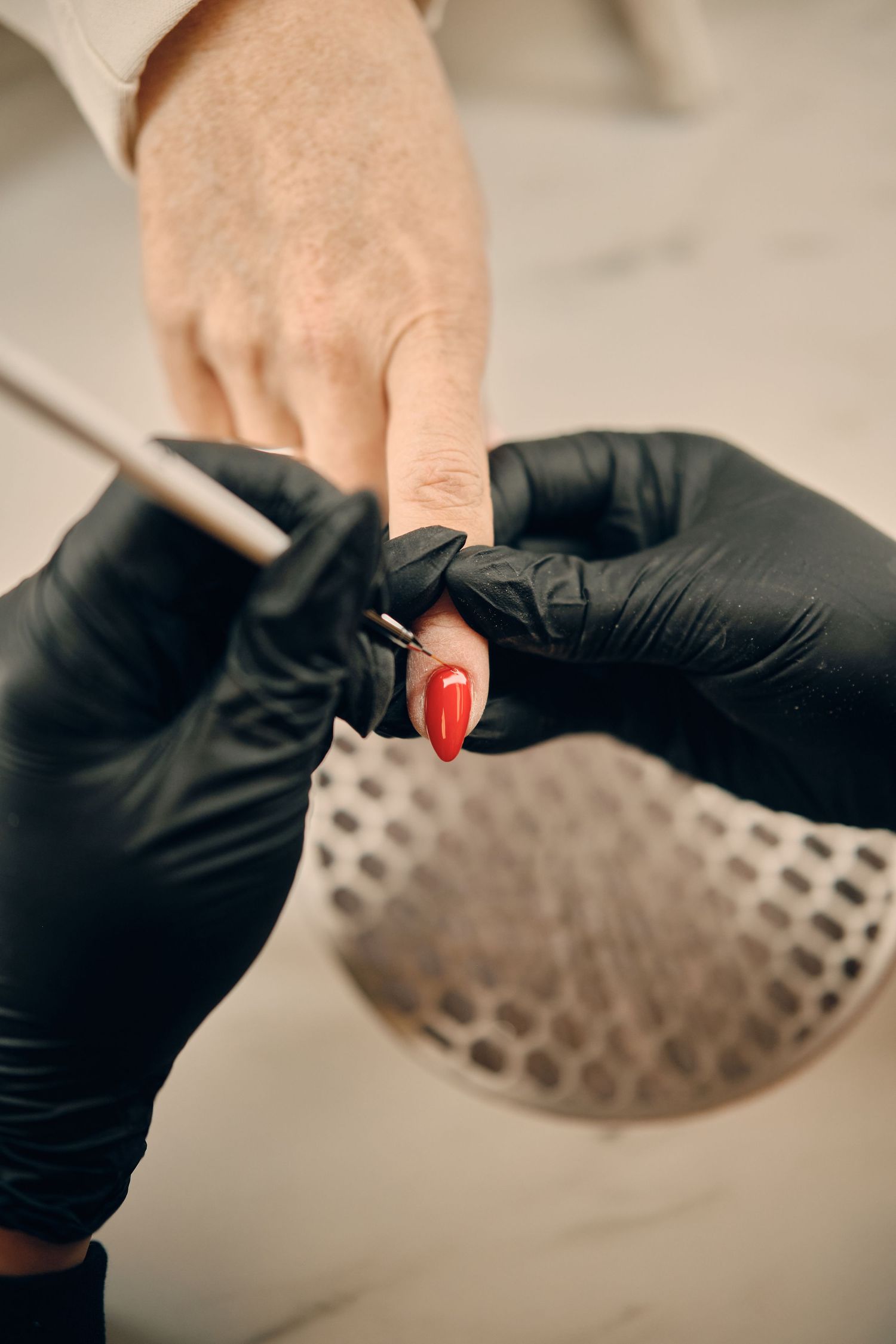Nail technician in black gloves applying red gel polish to a client's fingernail during a professional manicure.