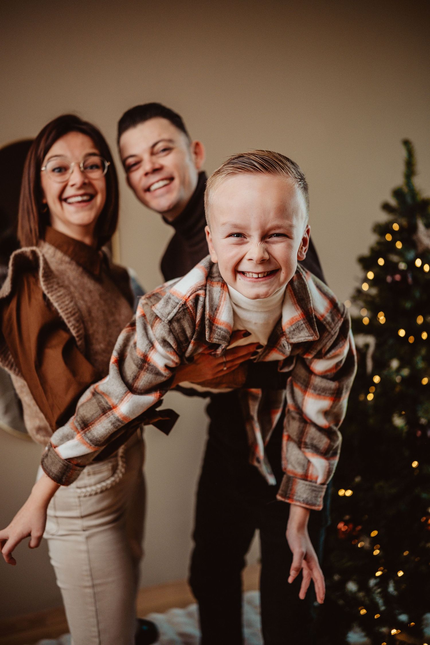 A playful holiday photo series showing a family having fun in front of a Christmas tree in warm brown tones.
