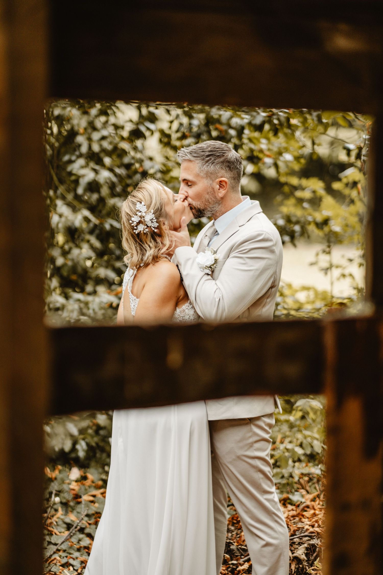 Couple in wedding attire share an intimate moment in a wooded setting.