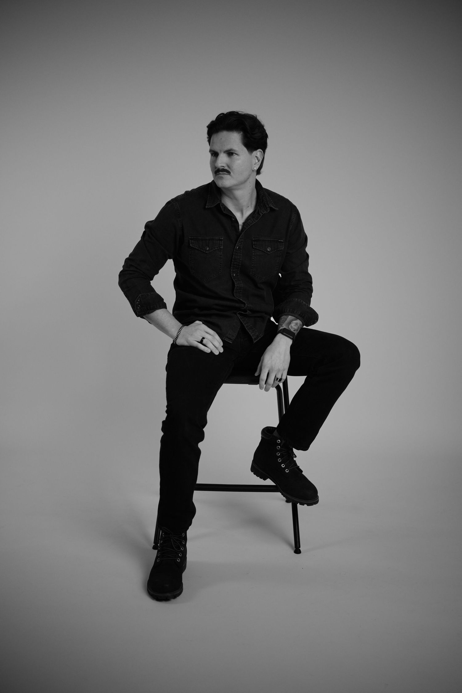 Black and white portrait series showing someone in dark clothing sitting on a chair in different poses against a plain backdrop.