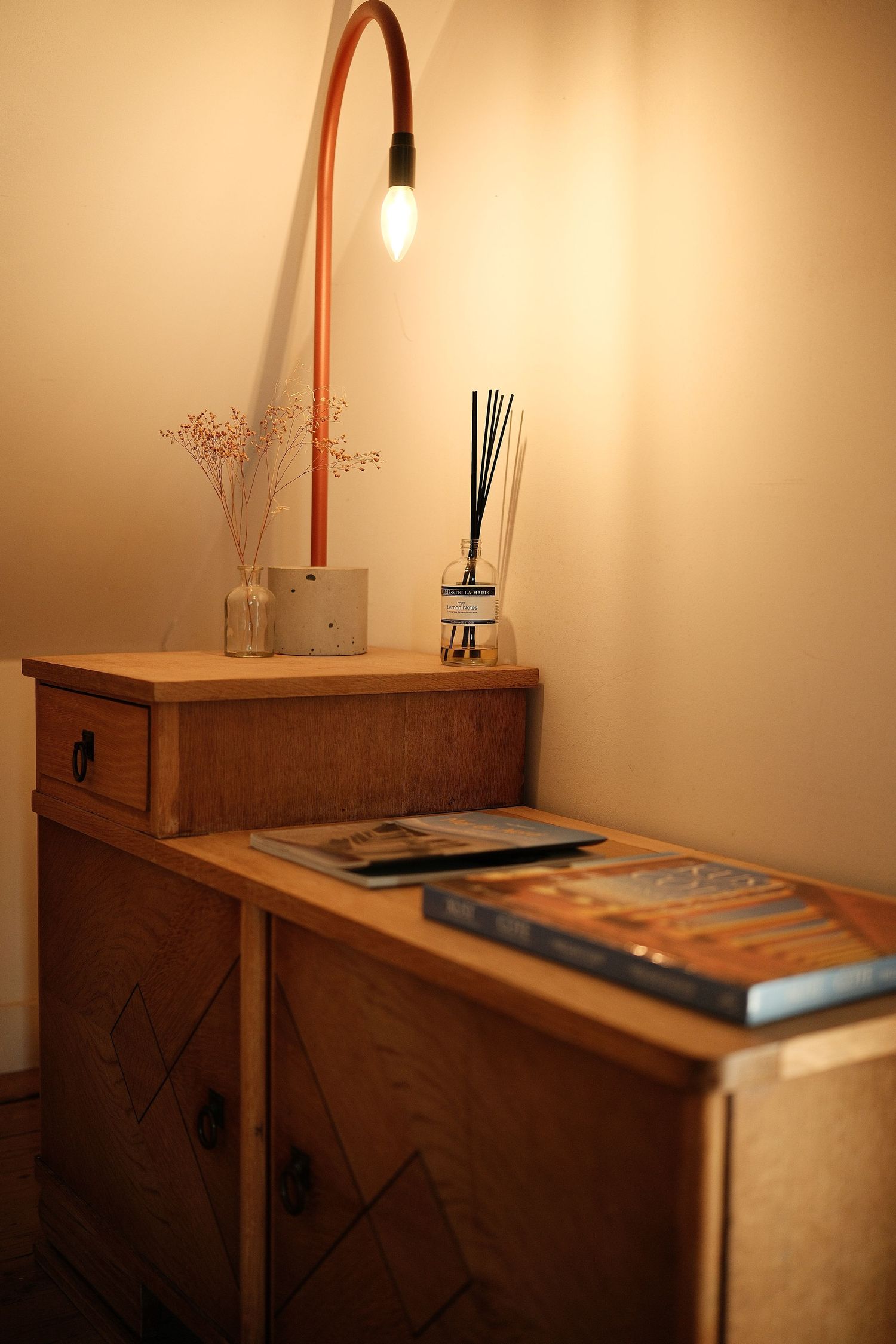 Wooden dresser with lamp and decorative items in warm-lit room.