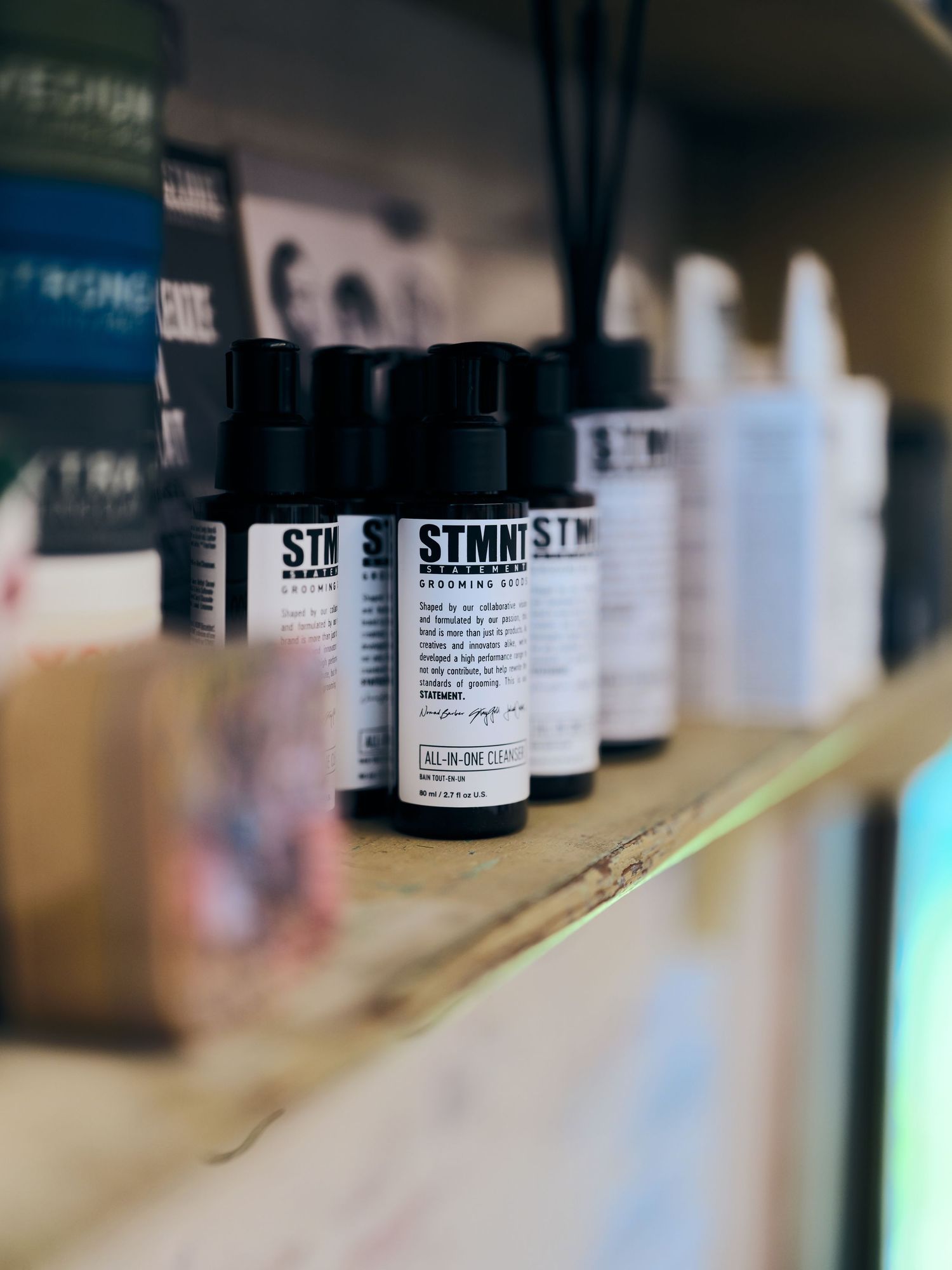 STMNT grooming goods products displayed on a wooden shelf in a barbershop retail setting.