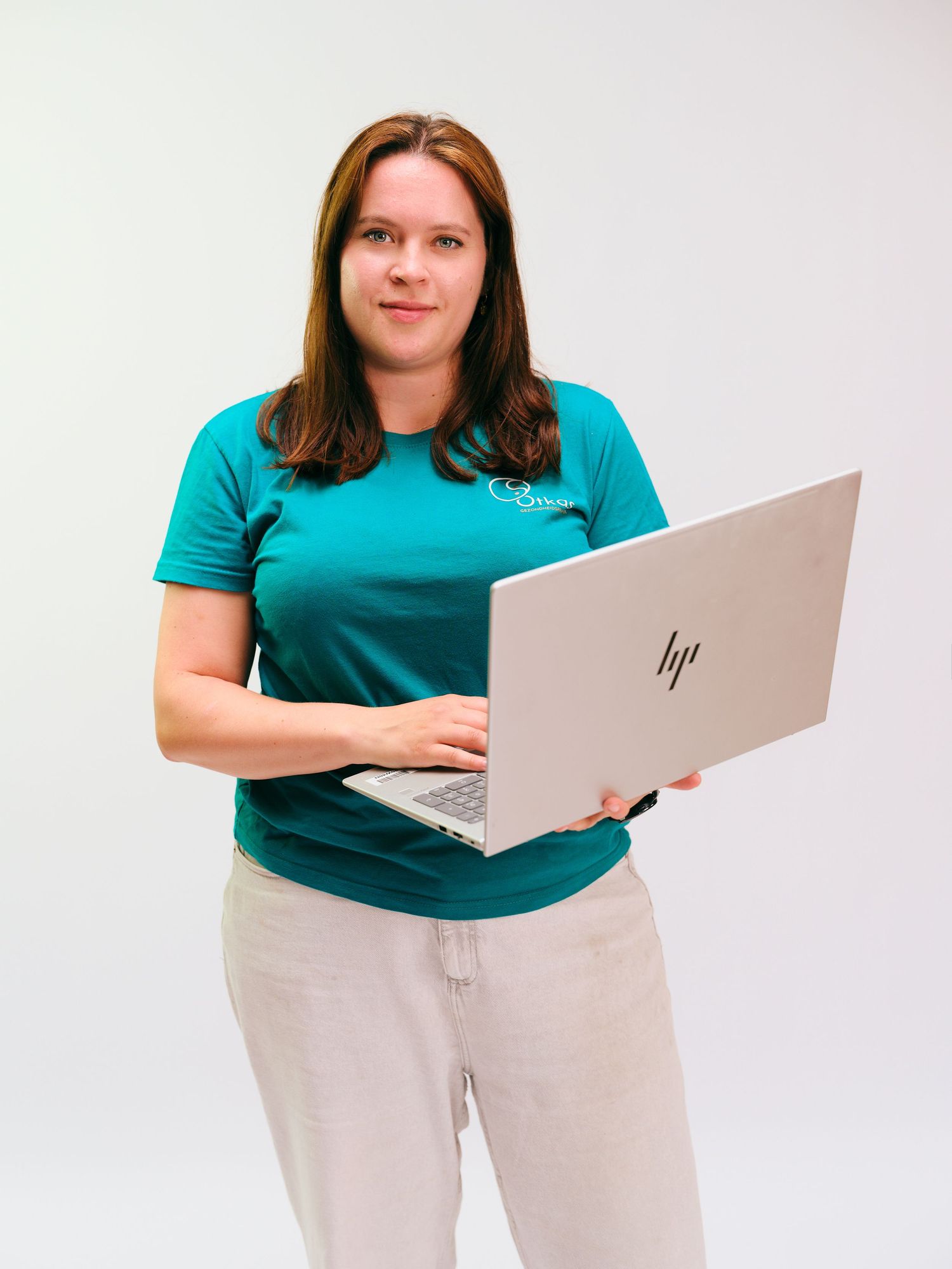 Woman in teal t-shirt holding HP laptop, standing against white background, smiling confidently.
