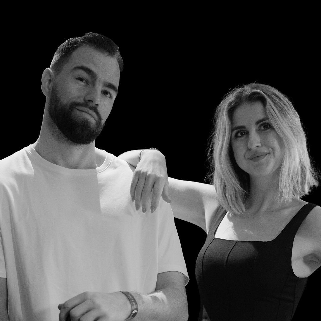 Black and white portrait of a bearded man in white t-shirt and blonde woman in black top posing together.