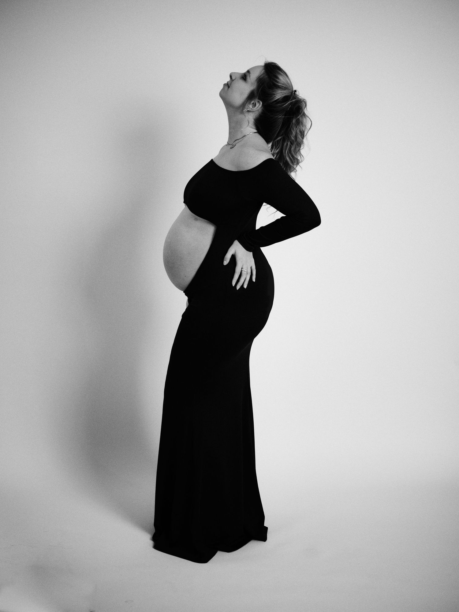Black and white maternity photography series showing silhouette of pregnant figure in flowing dress against light background.