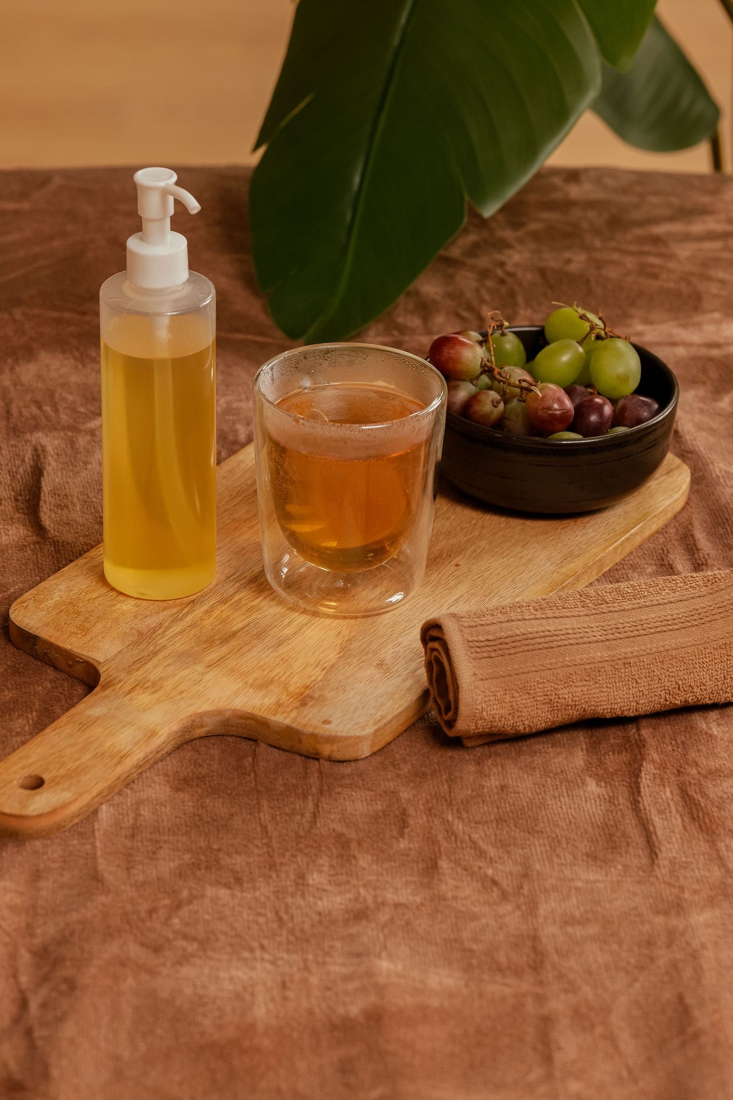 Spa setup with massage oil, tea, and fresh grapes on a wooden cutting board.