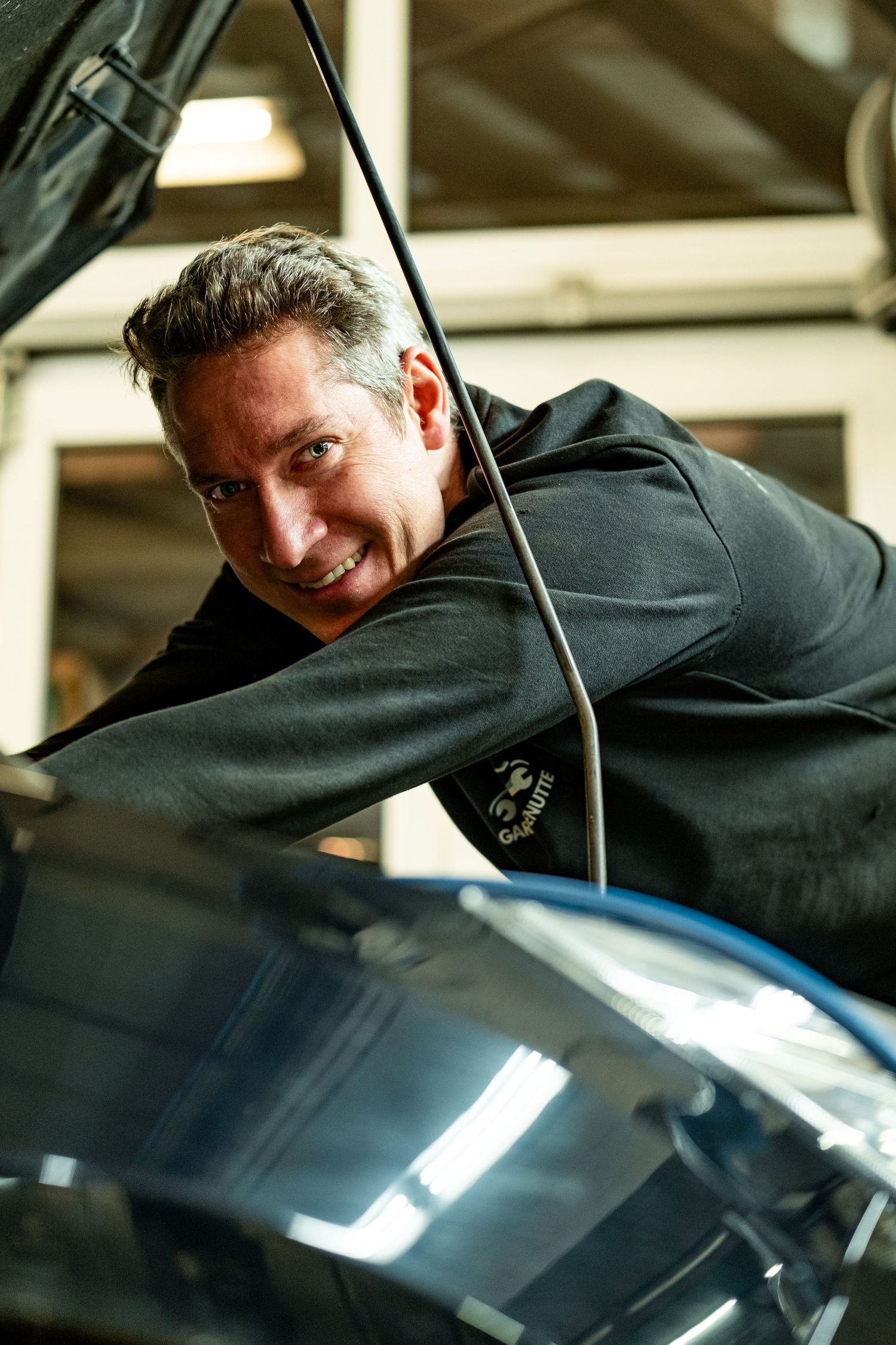 A person in black clothing leans over a shiny car surface while detailing or inspecting the vehicle's finish.