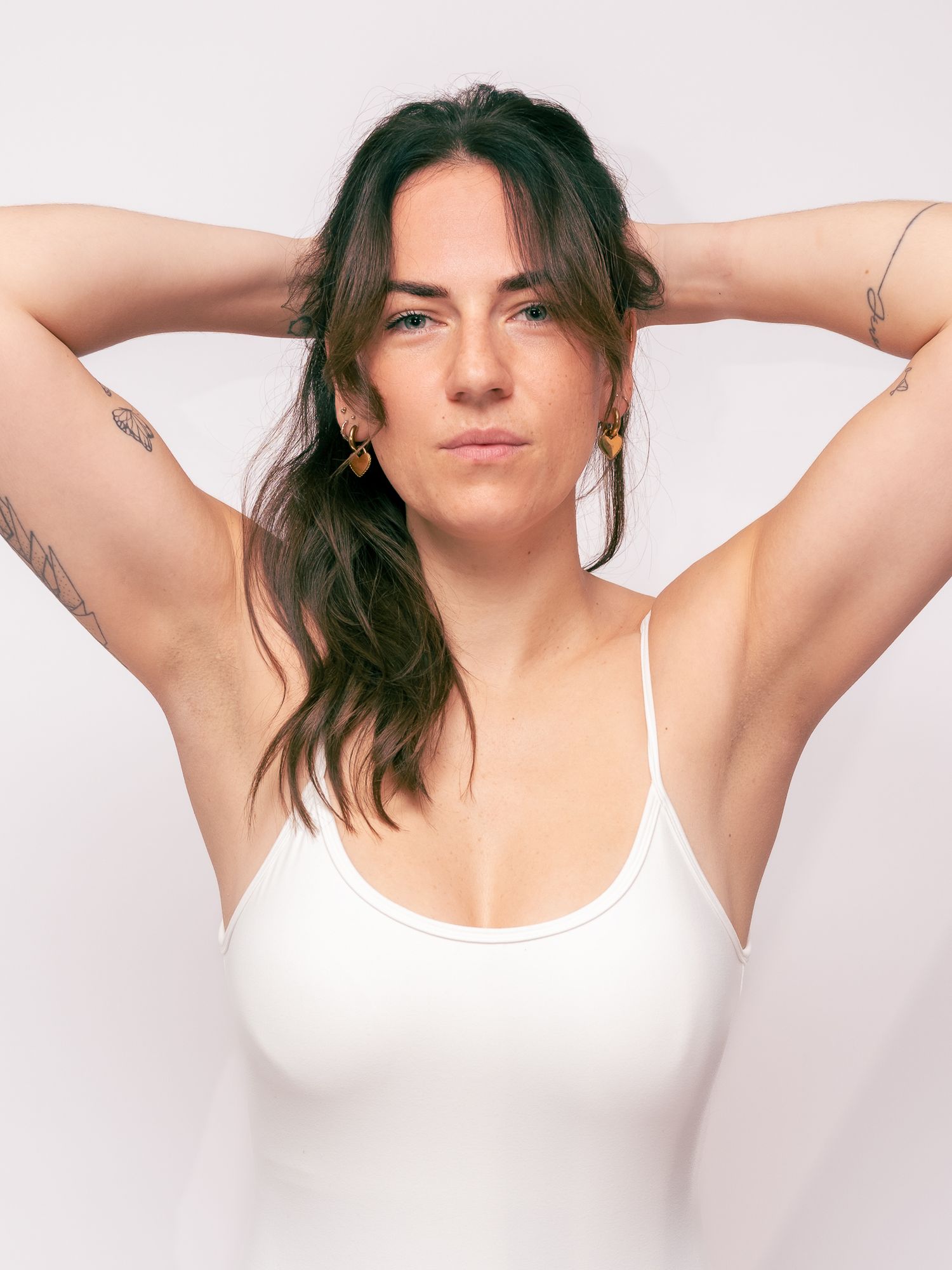 Person in white tank top with arms raised in artistic portrait series.