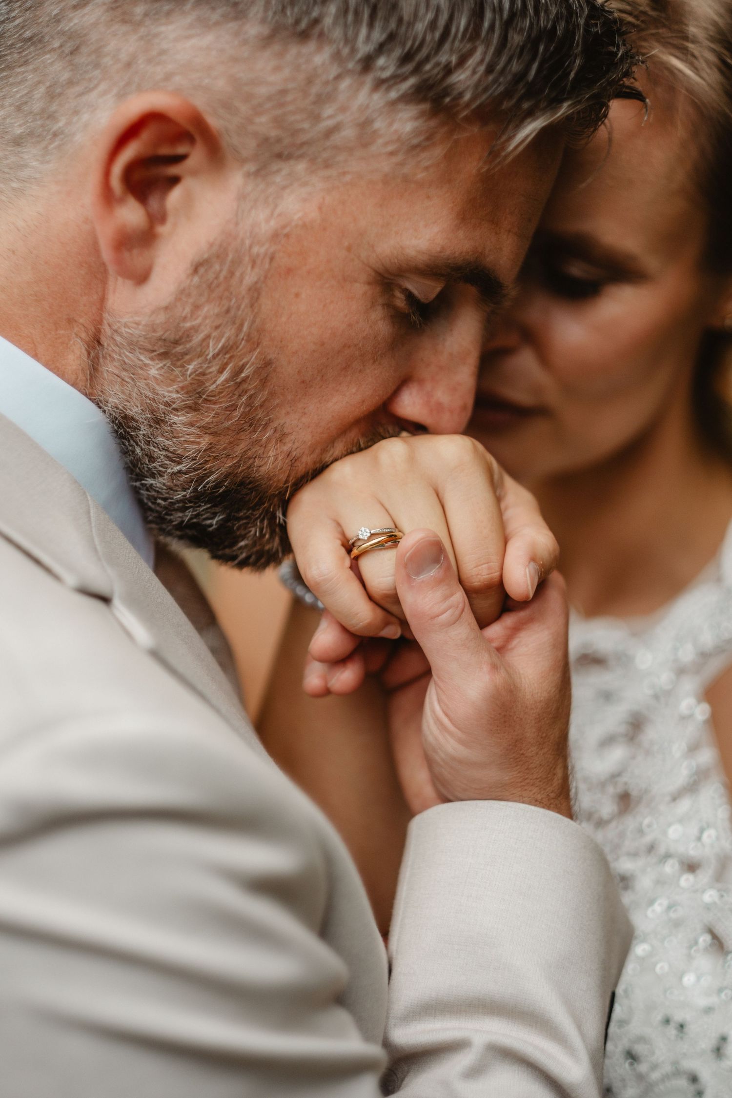 Close-up of tender wedding moment with rings visible.