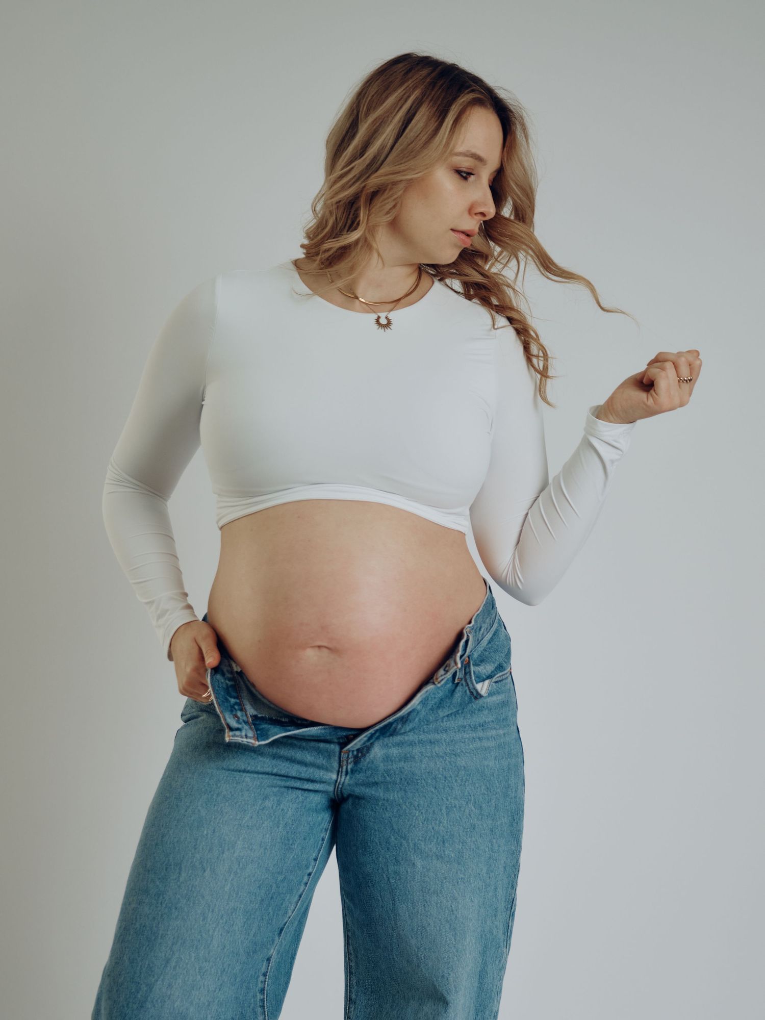 A series of pregnancy progression photos showing a growing baby bump in white top and blue jeans against a light background.