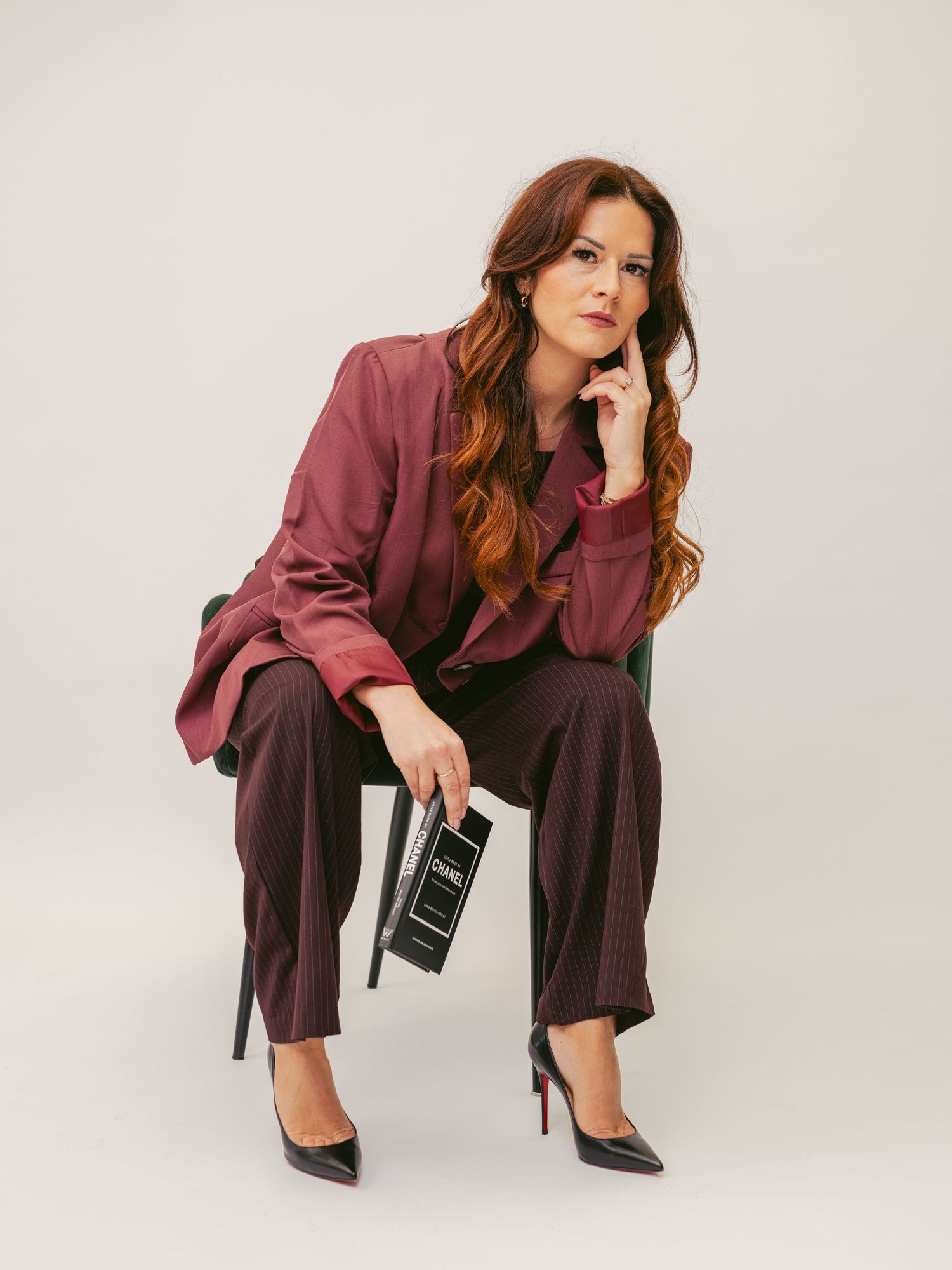 Fashion model in burgundy blazer and dark pants poses dramatically against white background in studio setting.