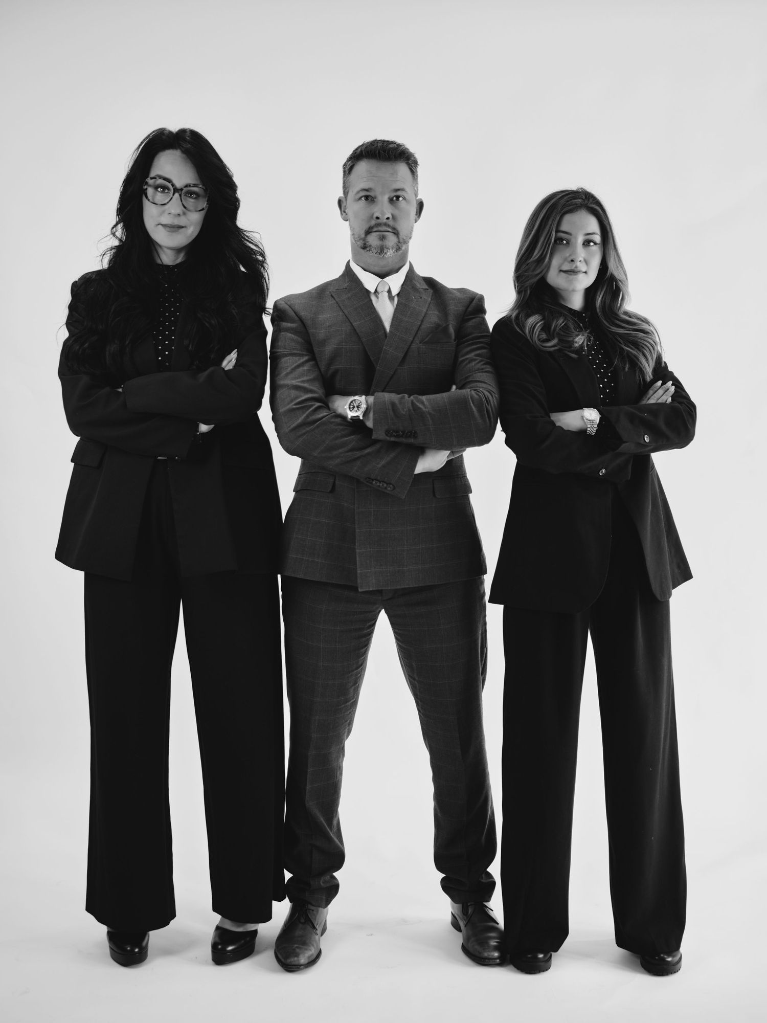 Three professionals in black attire pose confidently with arms crossed in a black and white studio portrait.