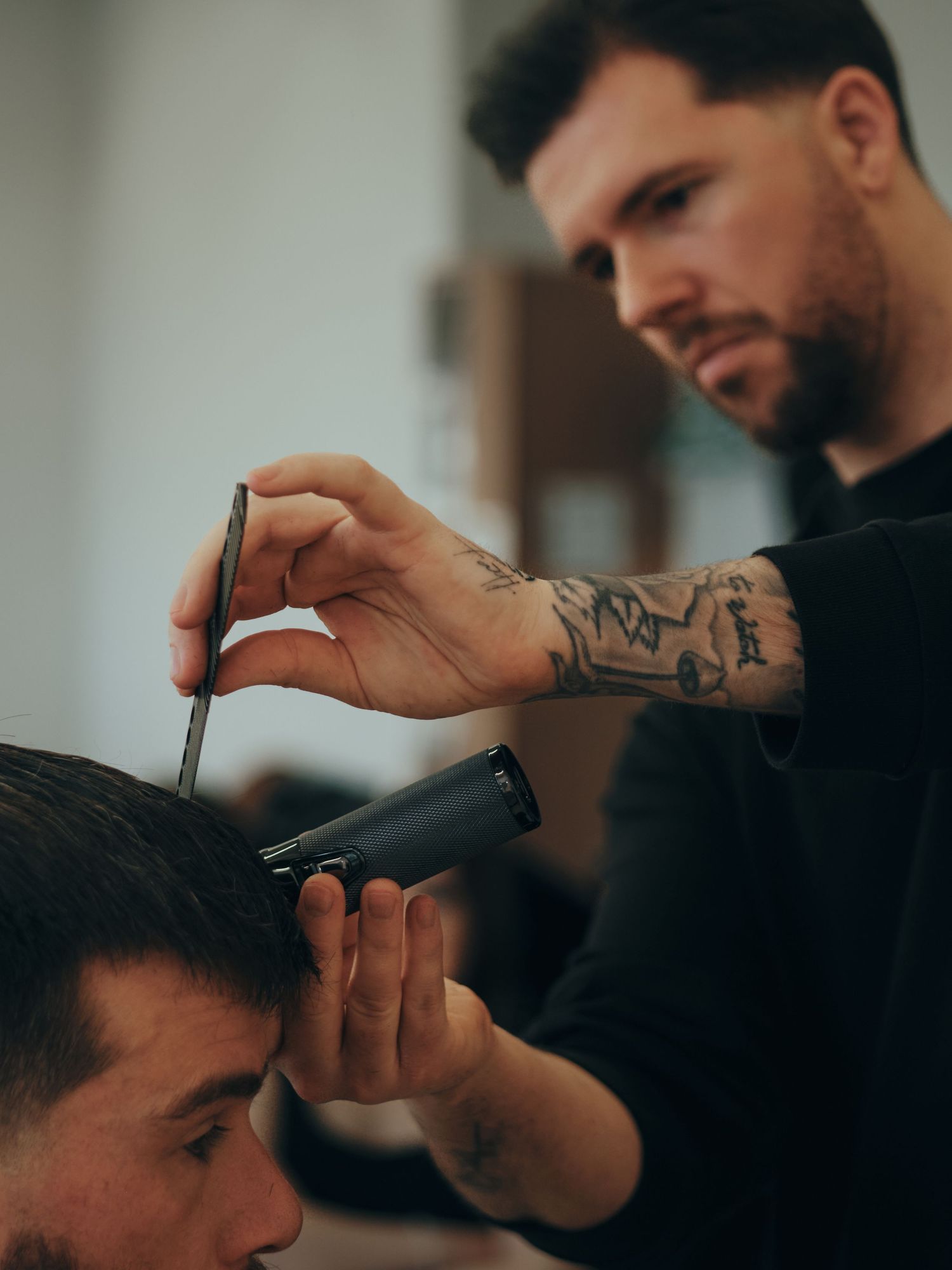 Tattooed barber cutting a male client's hair with scissors and clippers in a modern barbershop.