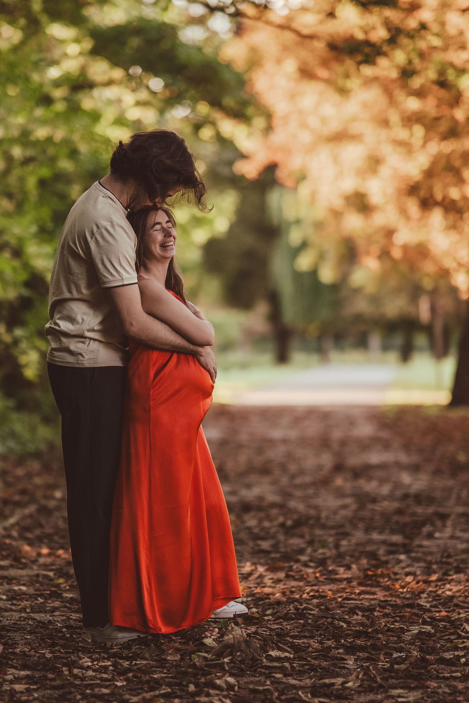 Romantic autumn maternity photos captured on a leaf-covered ground with warm golden lighting.