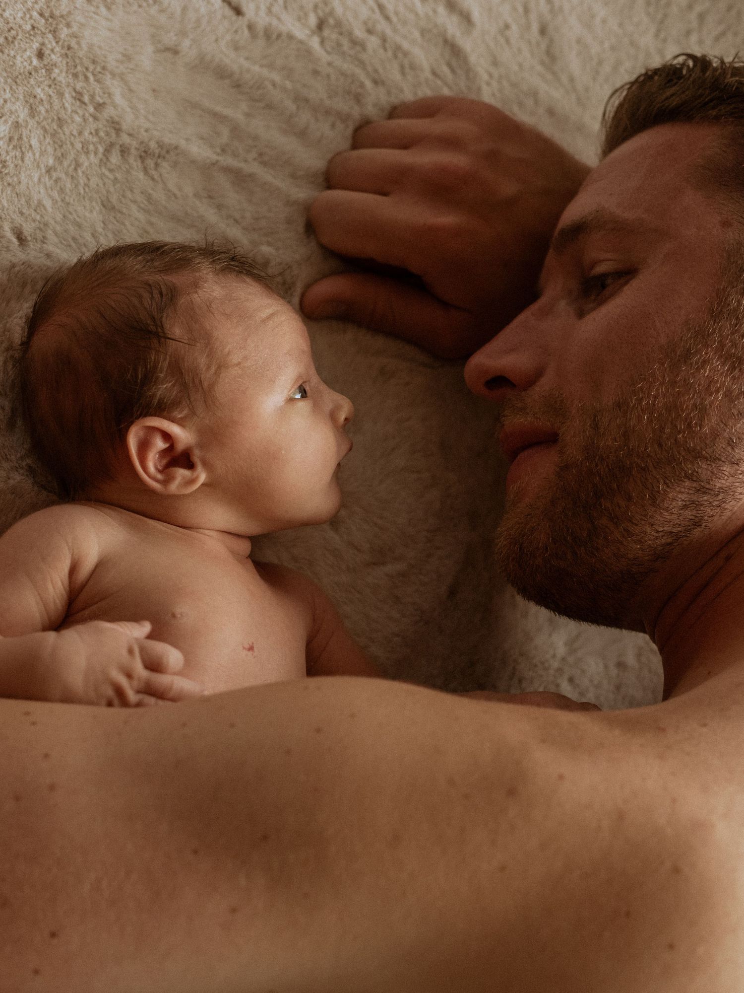 Tender moment between parent and infant lying together in warm sepia tones.