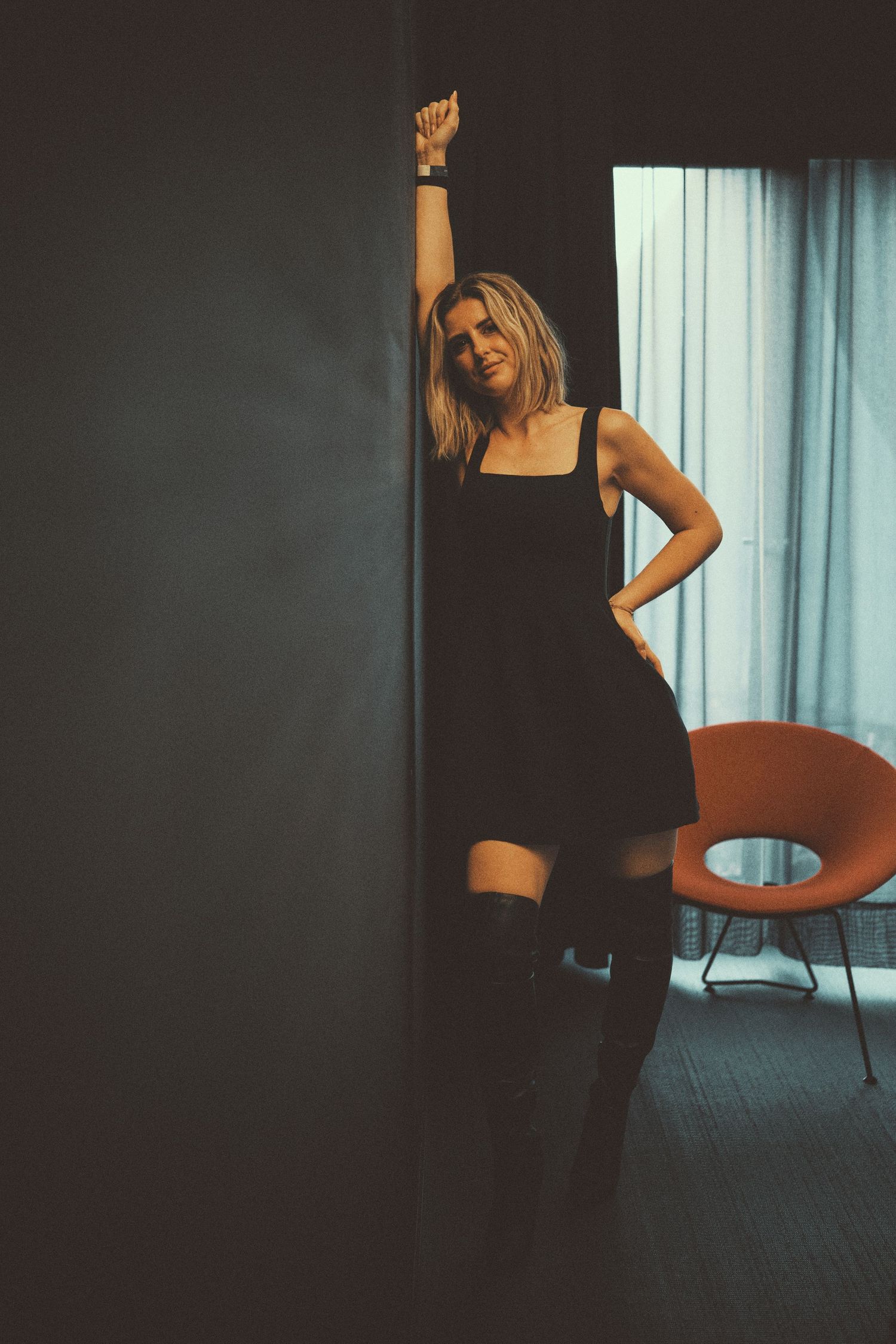 A silhouetted figure dances energetically in a dimly lit room with curtained windows in the background.
