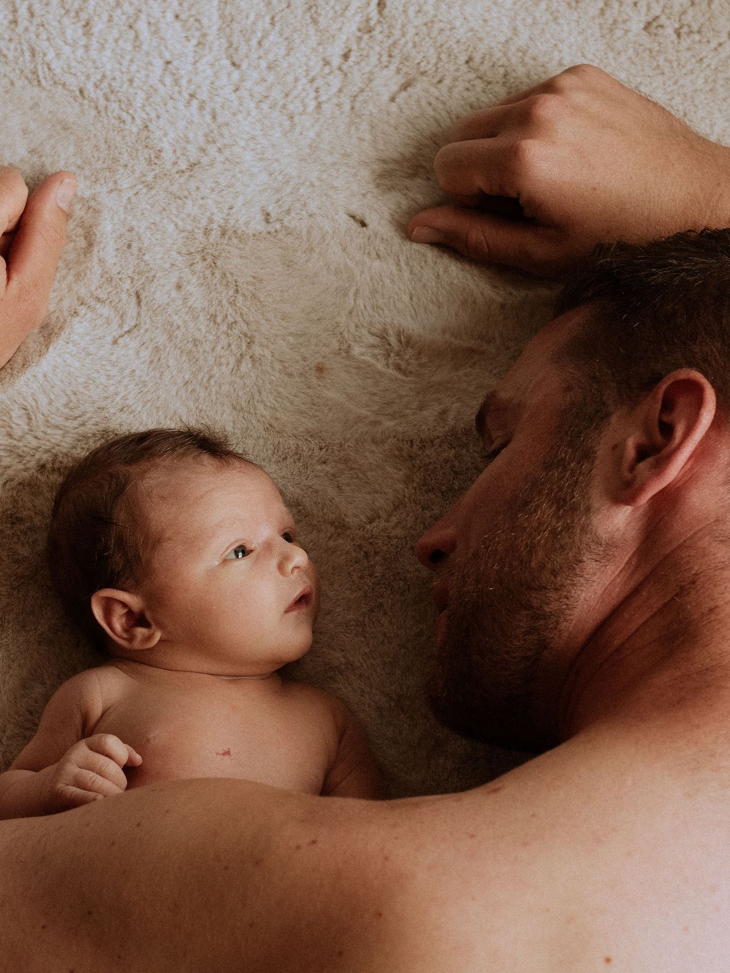 Intimate newborn photography session capturing tender parent-child moments on textured background.