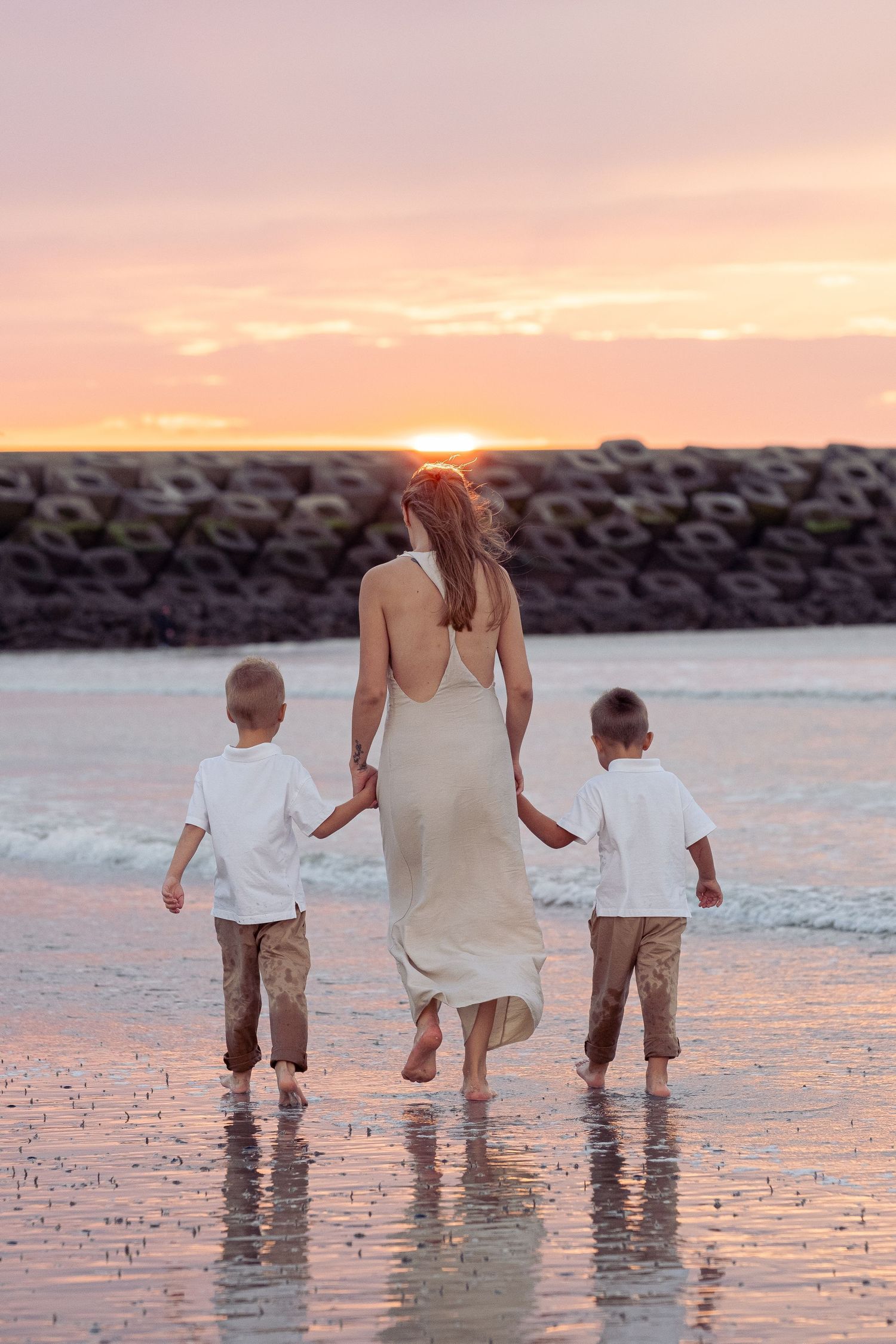 Family walking together on wet beach sand during a beautiful pink sunset.
