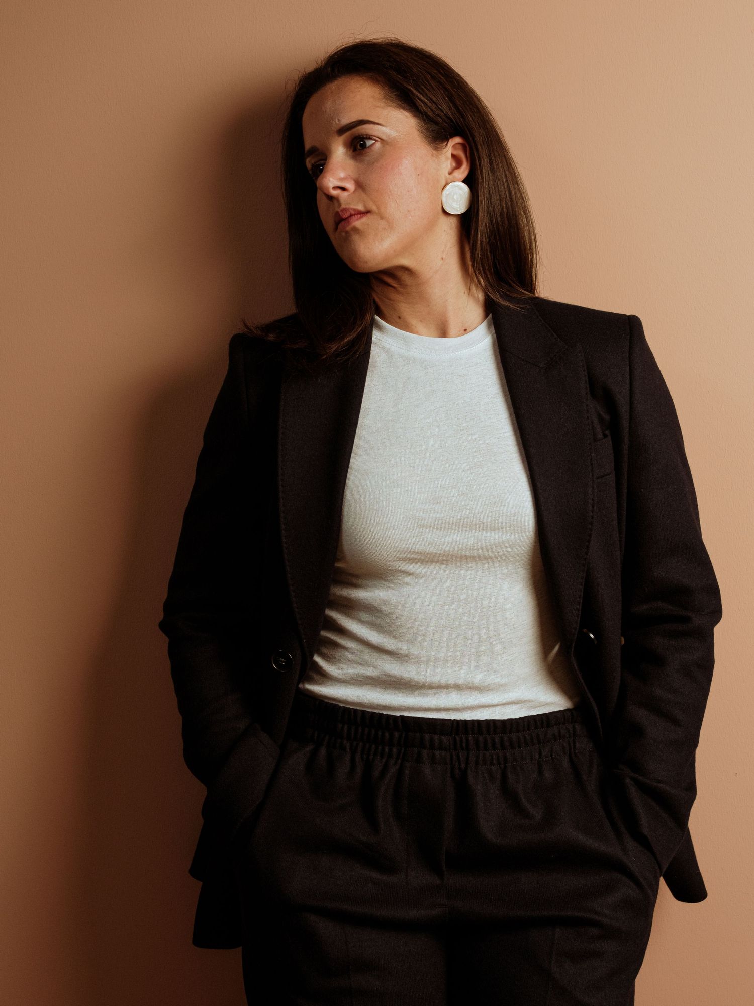 A fashion model in a white top and black blazer poses against a beige background in a series of editorial shots.
