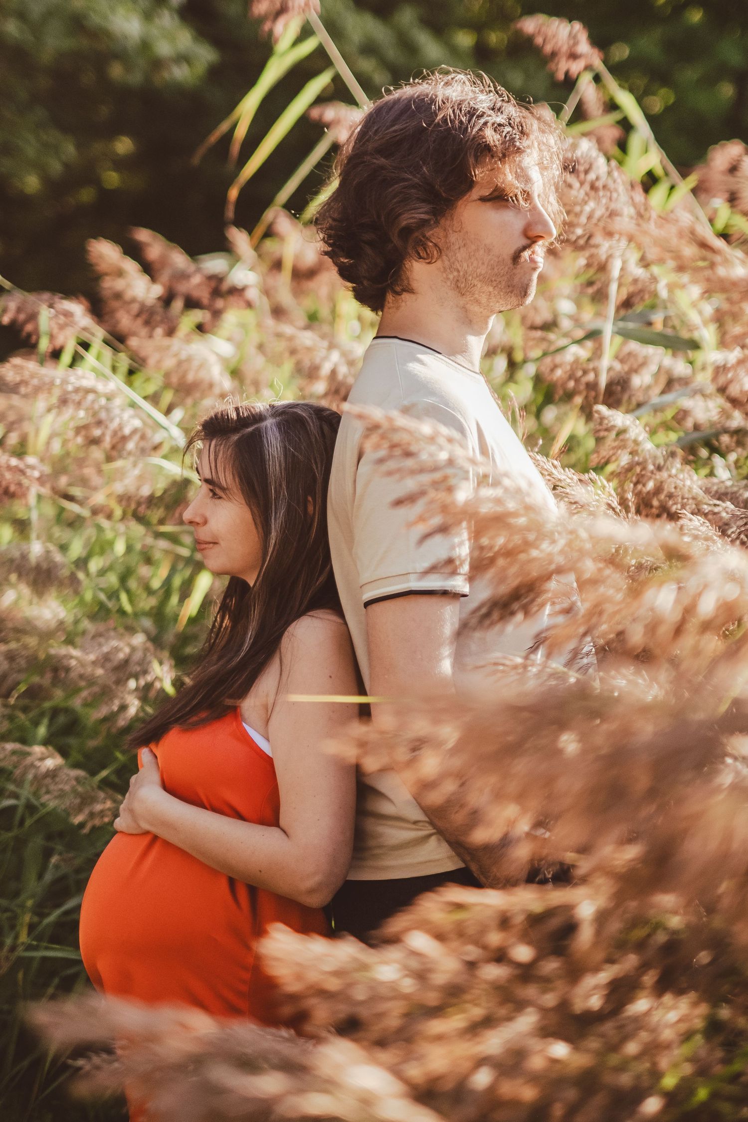 Intimate maternity photoshoot in a garden with soft lighting and pink flowers in the foreground.