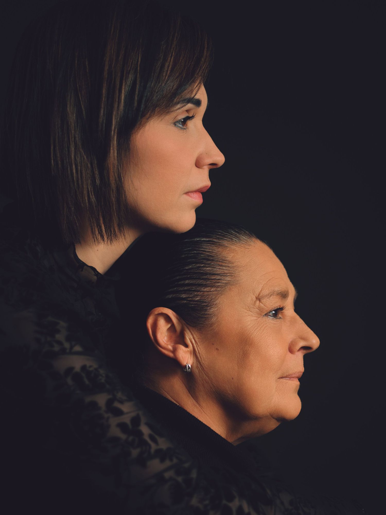 Two women in profile portrait, younger and older, against dark background, dramatic studio lighting.