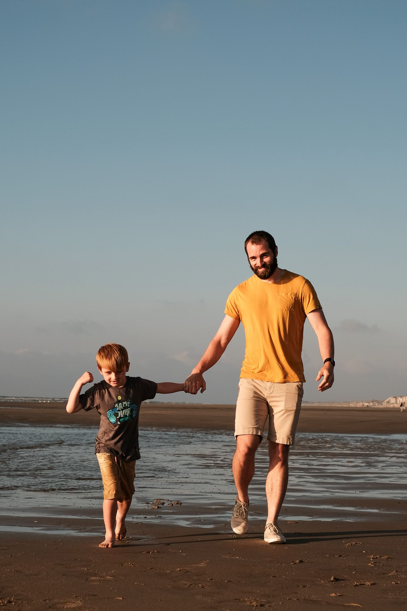 Parent and child walking together on a beach at sunset while exploring the shoreline.