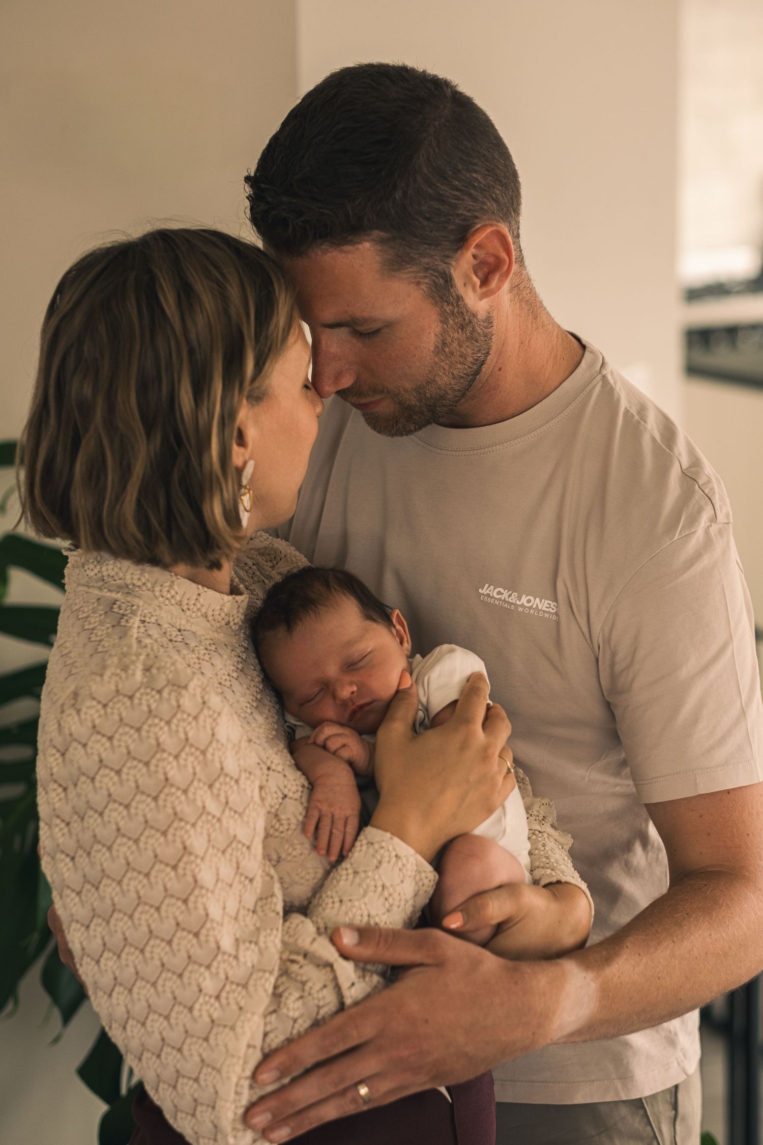 Parents cradling newborn baby together in warm indoor lighting.