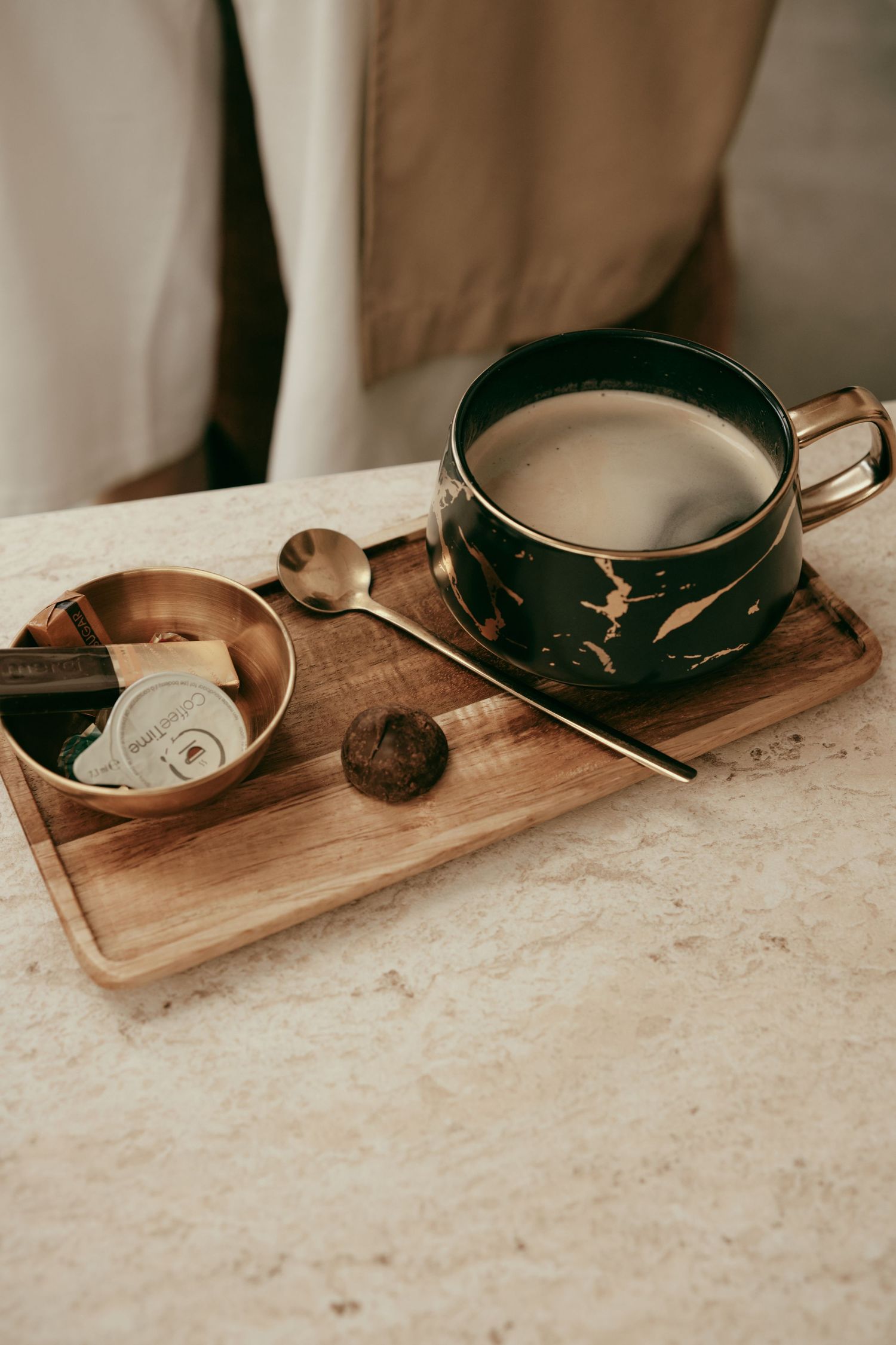 Elegant marble and gold cup of coffee on wooden tray with brass bowl, spoon, and chocolate truffle.