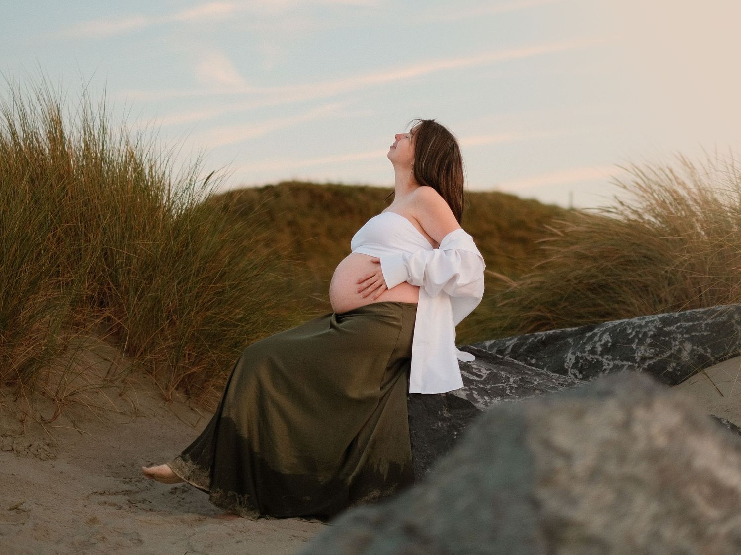 Dreamy maternity photoshoot in coastal dunes with soft lighting.