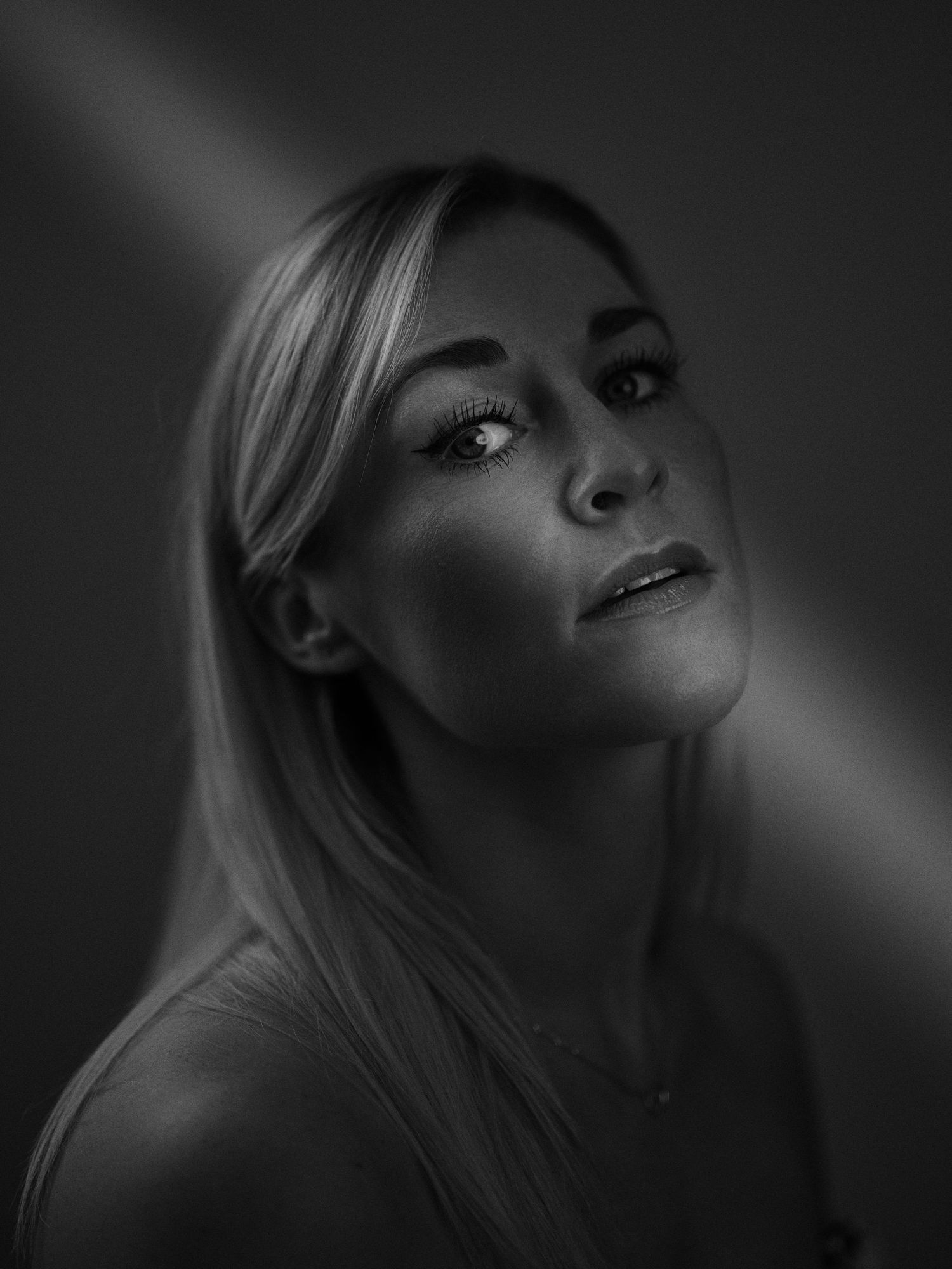 Black and white portrait of a blonde woman with dramatic lighting, gazing upward against a dark background.