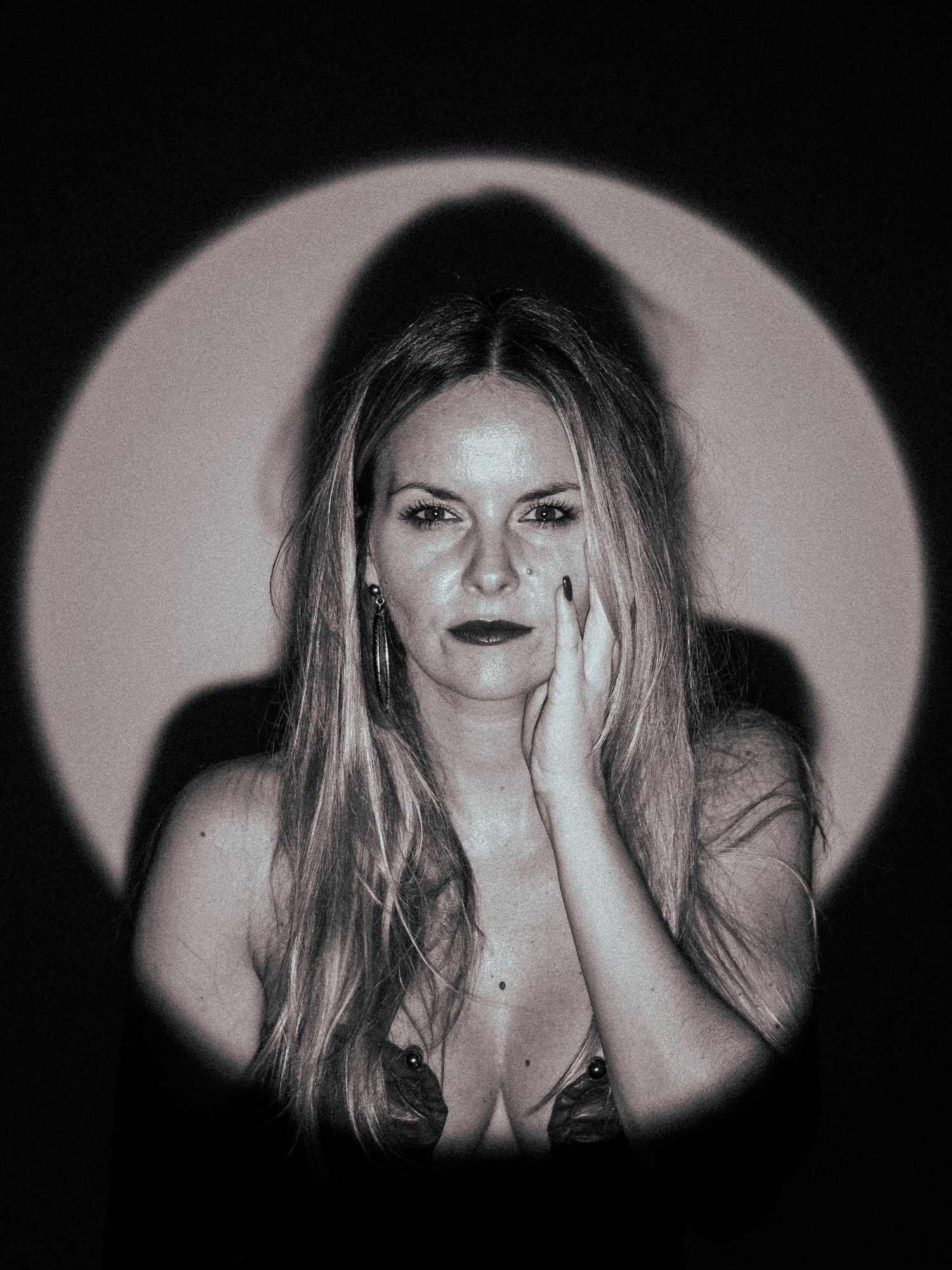 Black and white portrait of a blonde woman with long hair posing thoughtfully with hands near her face in dramatic lighting.