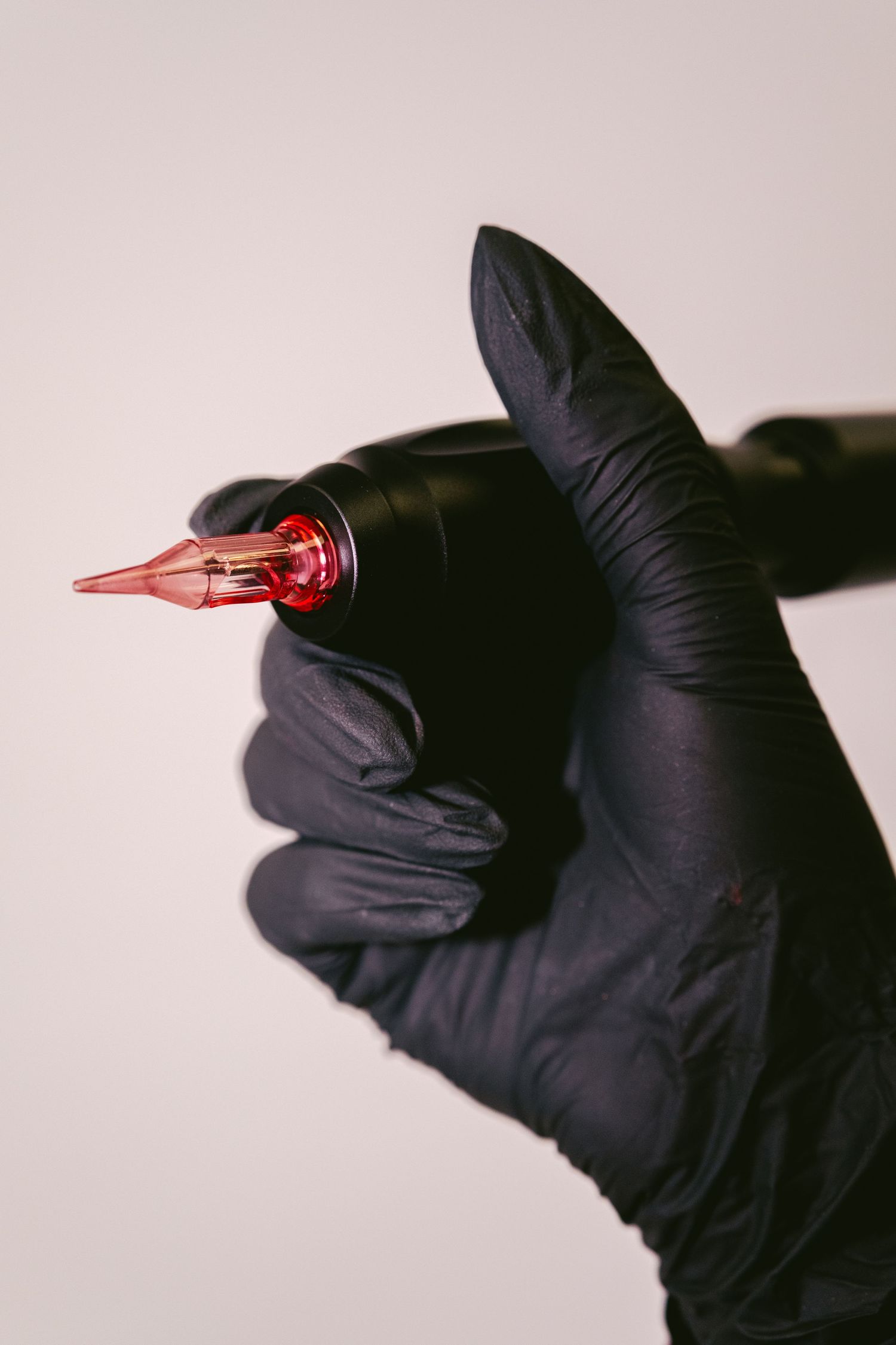 Black gloved hands holding a red medical syringe against a light gray background.