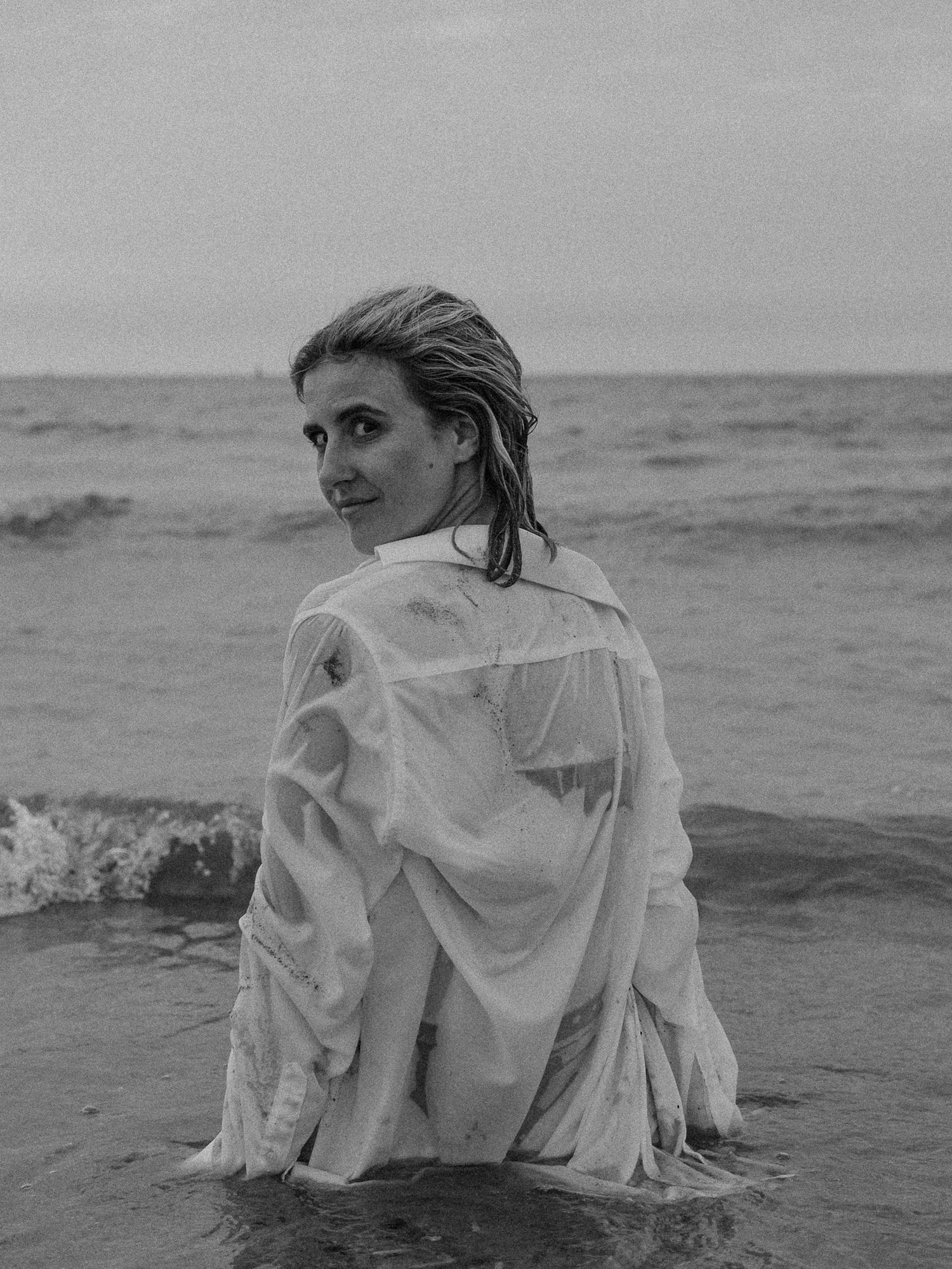 Ethereal beach photoshoot with flowing white fabric against ocean waves.
