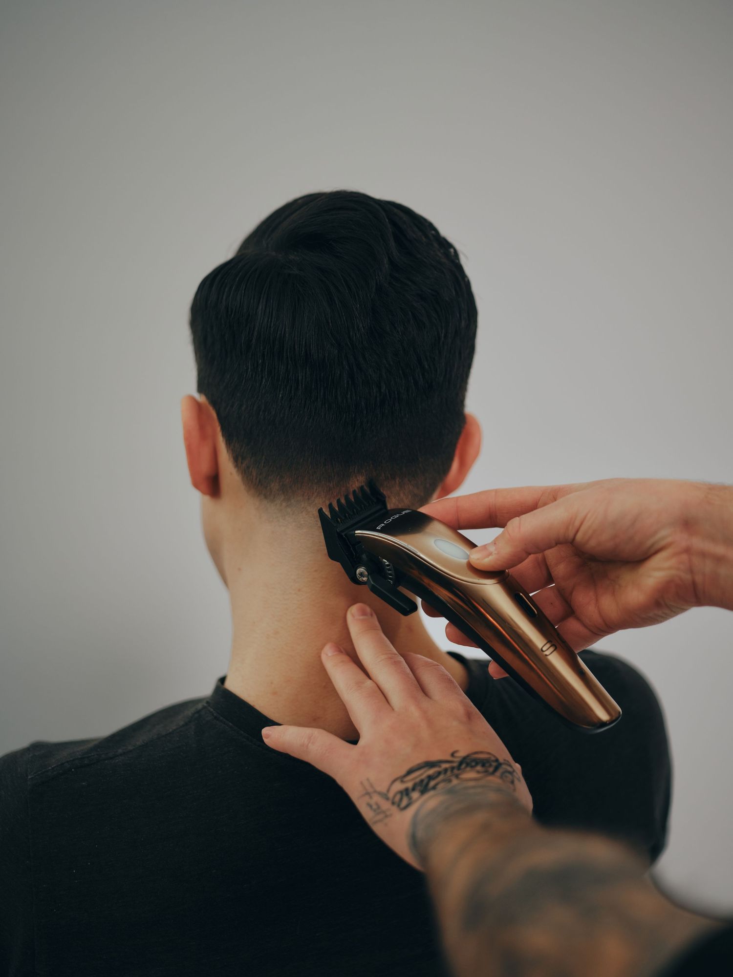 A professional haircut in progress showing multiple stages of trimming and styling with electric clippers on dark hair.