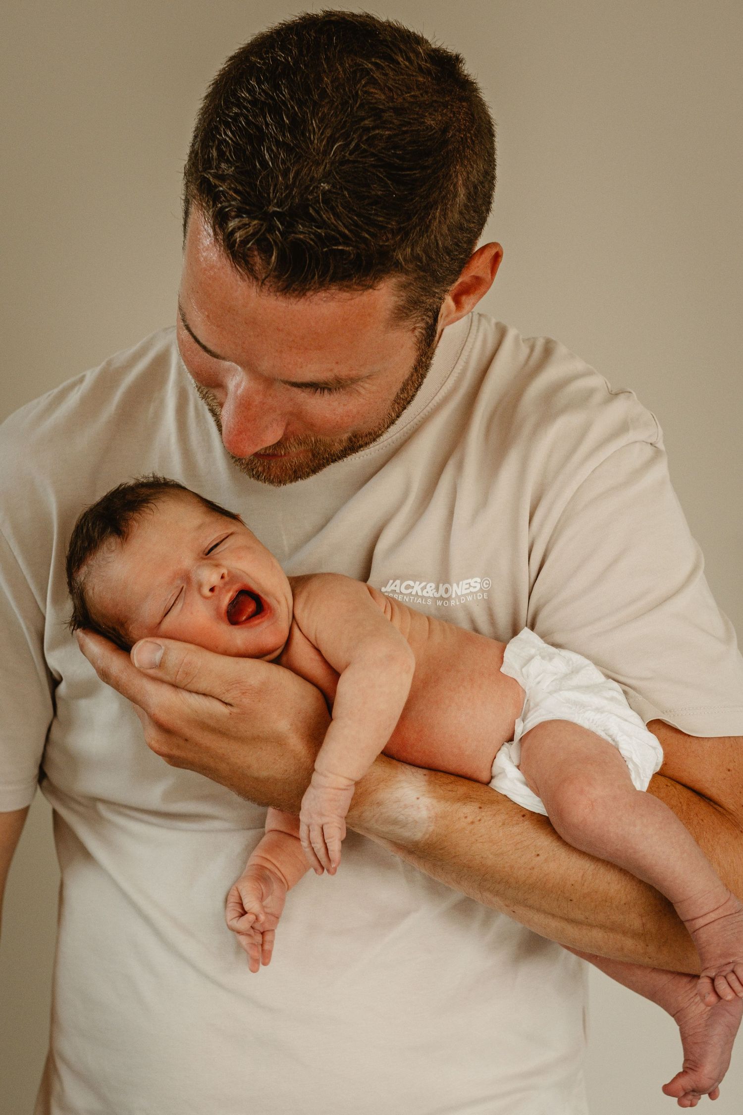 Parent in white shirt holding and kissing newborn baby in a series of natural portraits.