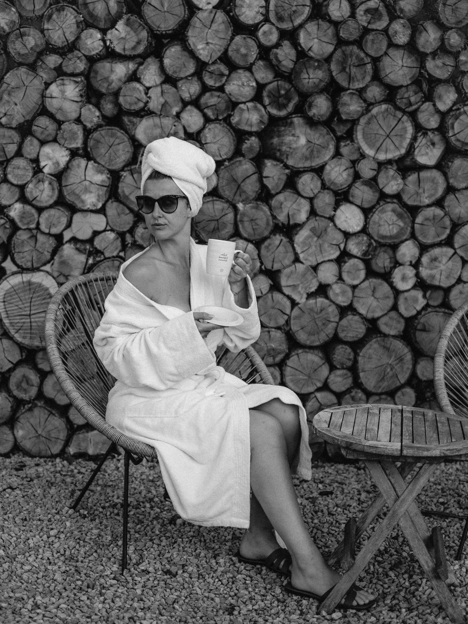 Black and white portrait of person in white clothing against stacked wood.